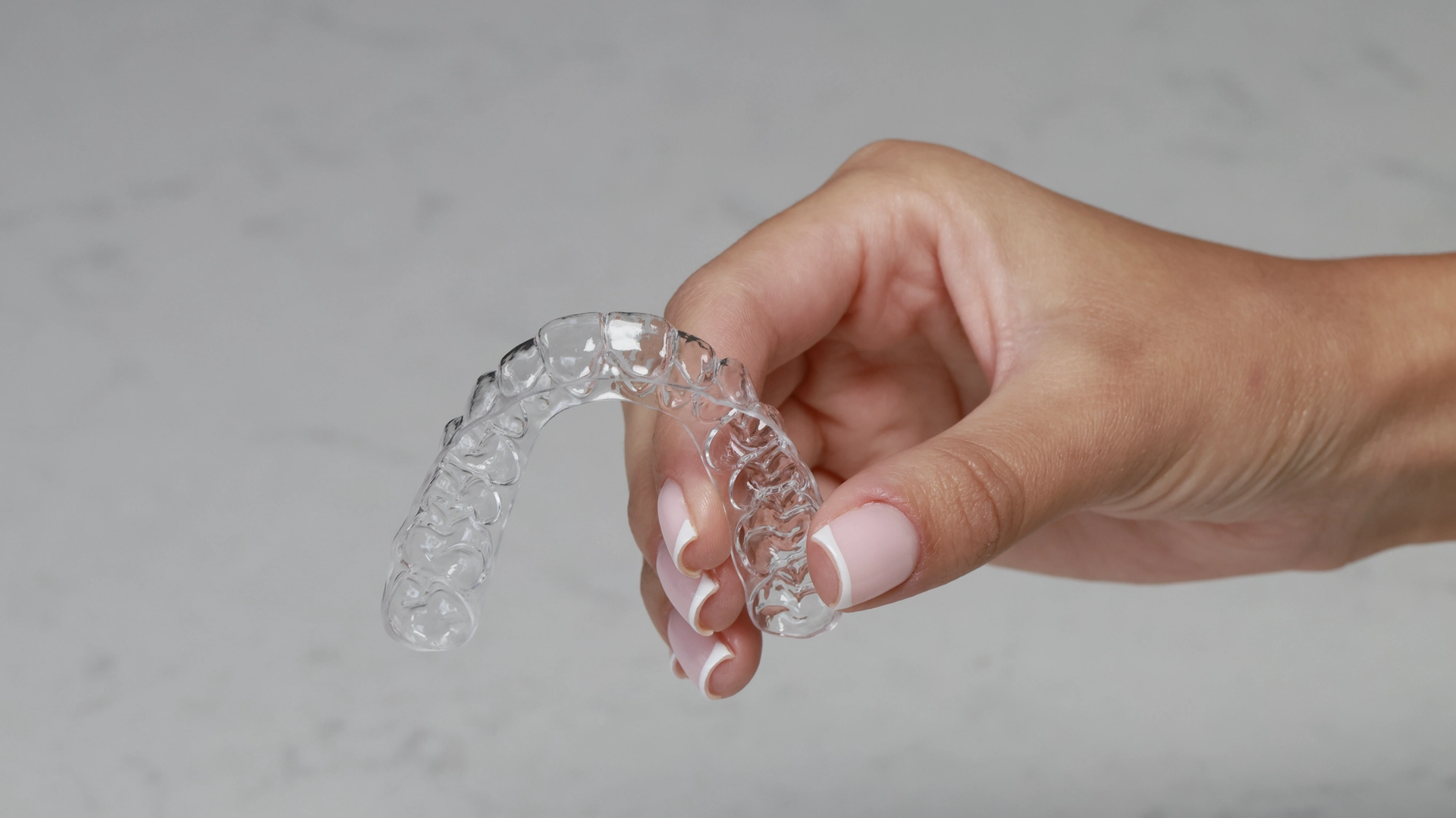 A hand holding a transparent clear aligner tray showing the detailed internal structure and tooth-tracking design used in orthodontic treatment.
