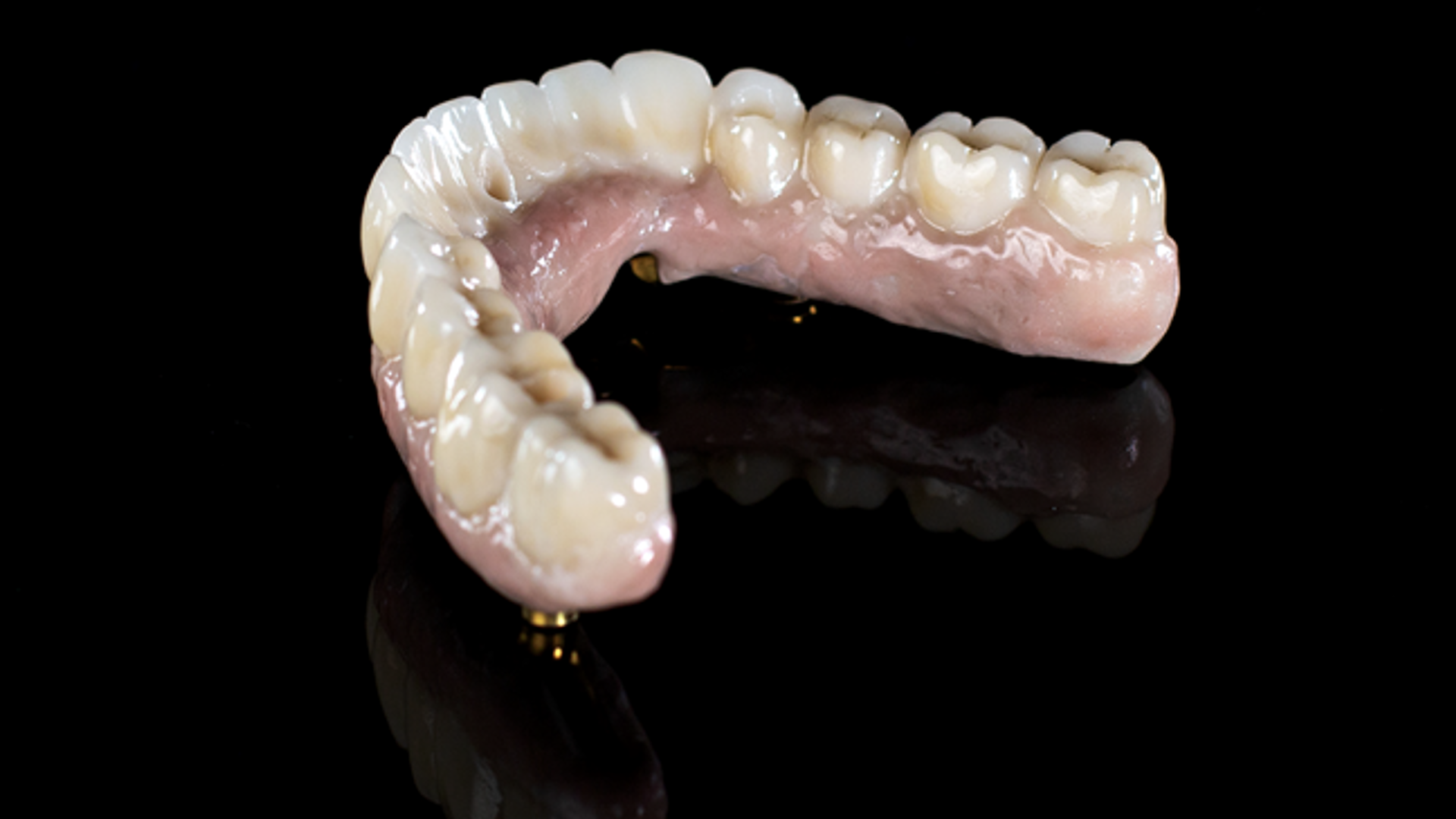 A complete maxillary and mandibular denture prosthesis with natural-looking ceramic teeth and pink acrylic base displayed against a black background.