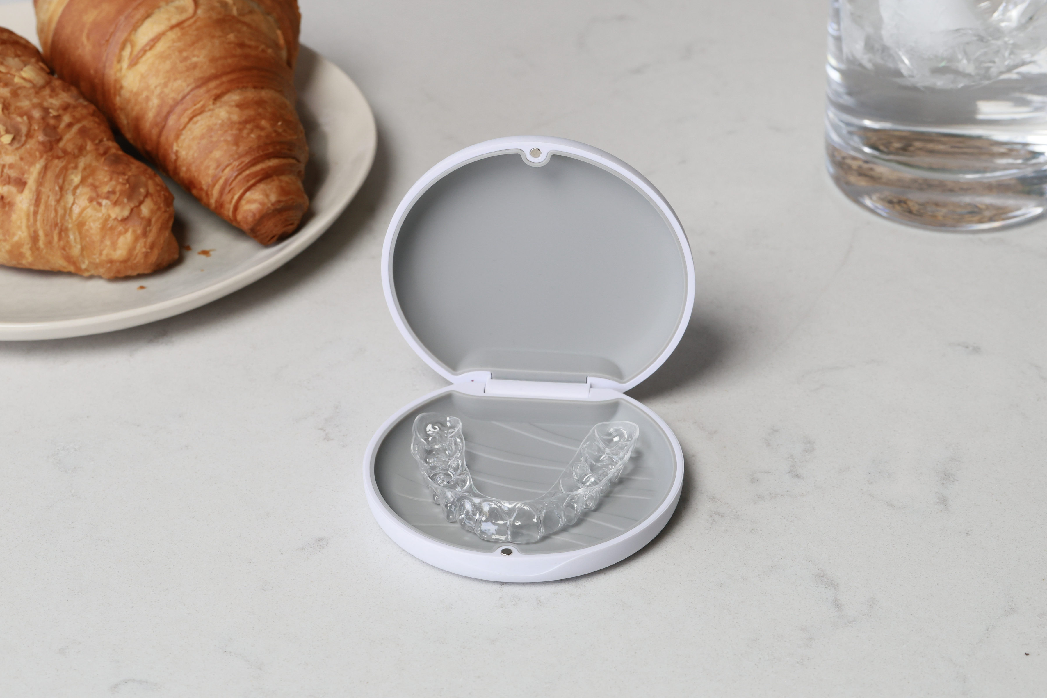 A pair of transparent orthodontic clear aligners displayed in an open white protective case on a marble surface.