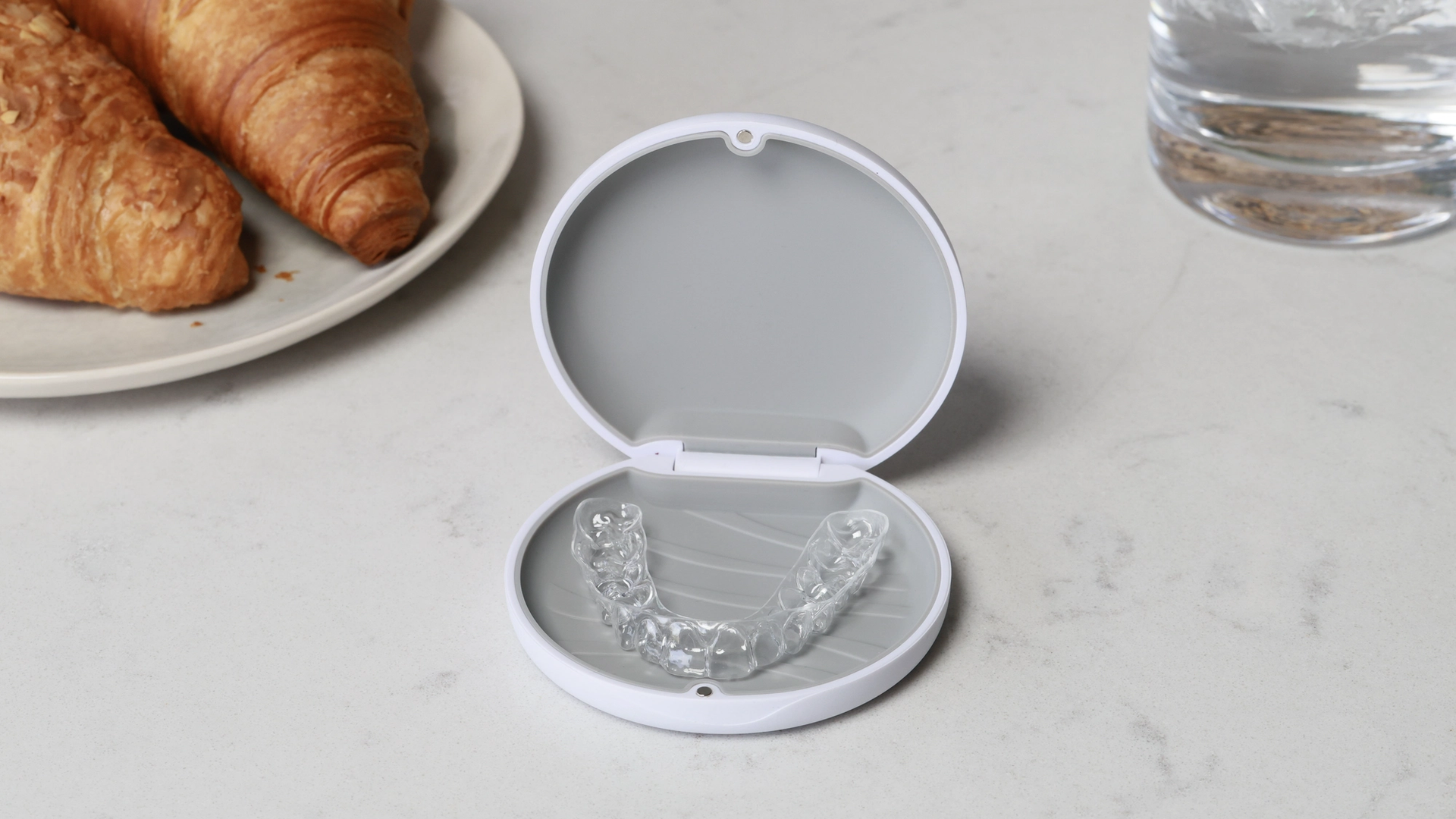 A pair of transparent orthodontic clear aligners displayed in an open white protective case on a marble surface.