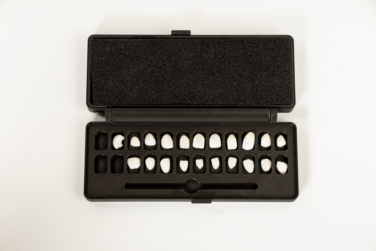 A black plastic case containing a complete set of tooth shade tabs arranged in two rows displaying various white and cream-colored dental crown or veneer samples for shade matching.