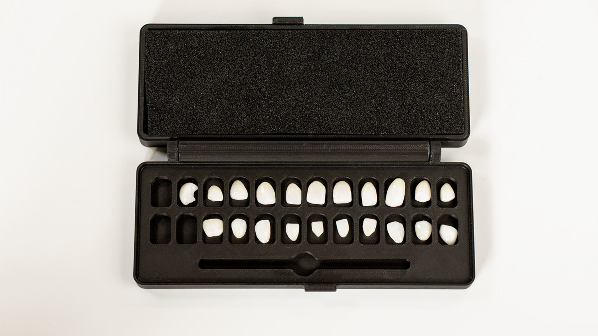 A black plastic case containing a complete set of tooth shade tabs arranged in two rows displaying various white and cream-colored dental crown or veneer samples for shade matching.