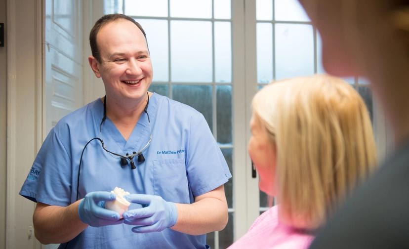 Image of a male clinician holding a dental model and smiling at a female patient