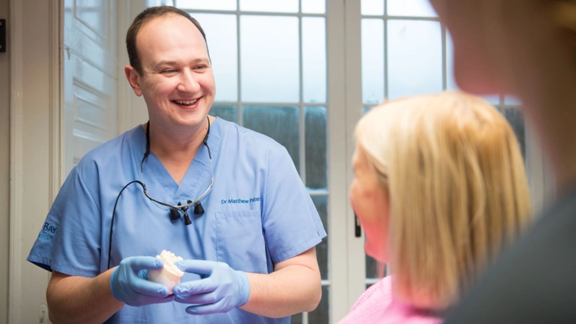 Image of a male clinician holding a dental model and smiling at a female patient