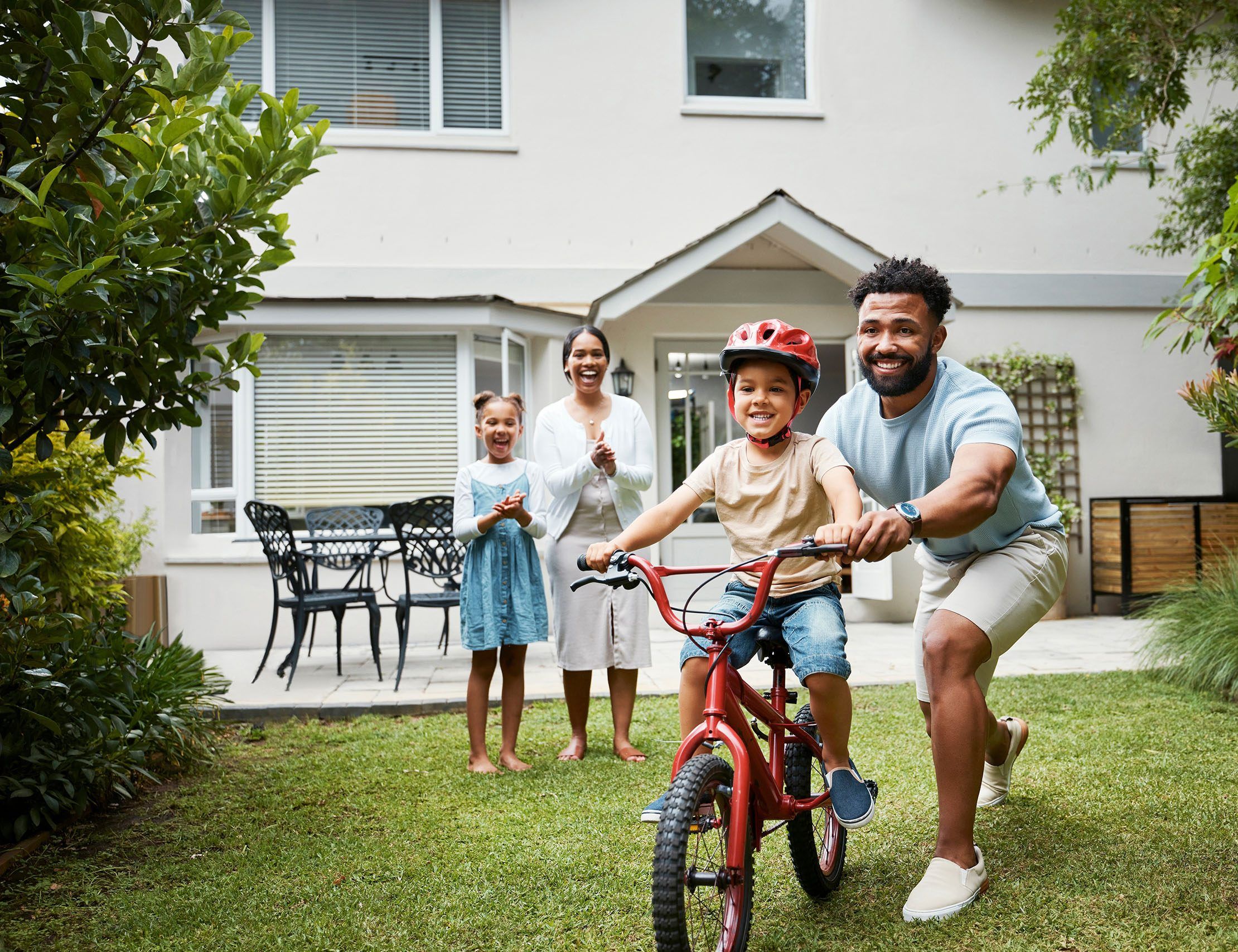 image of man showing child how to ride a bike whilst family watches on