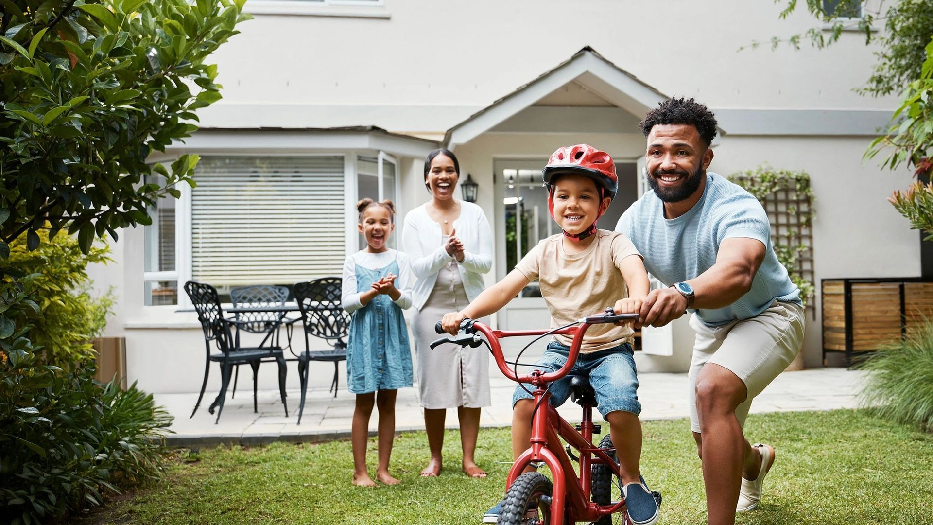 image of man showing child how to ride a bike whilst family watches on
