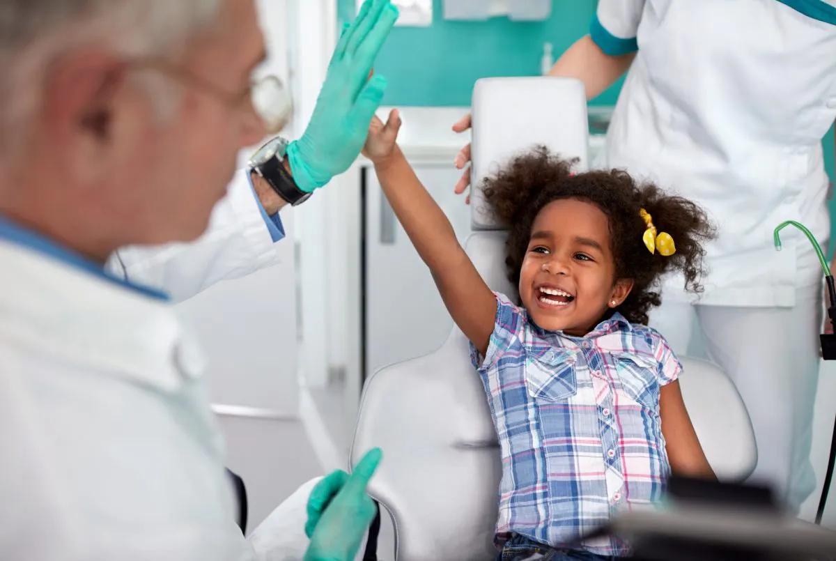 Image of a girl smiling ear to ear and giving a high five to a male dentist.