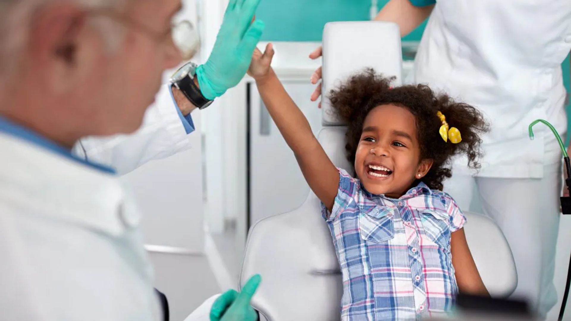 Image of a girl smiling ear to ear and giving a high five to a male dentist.
