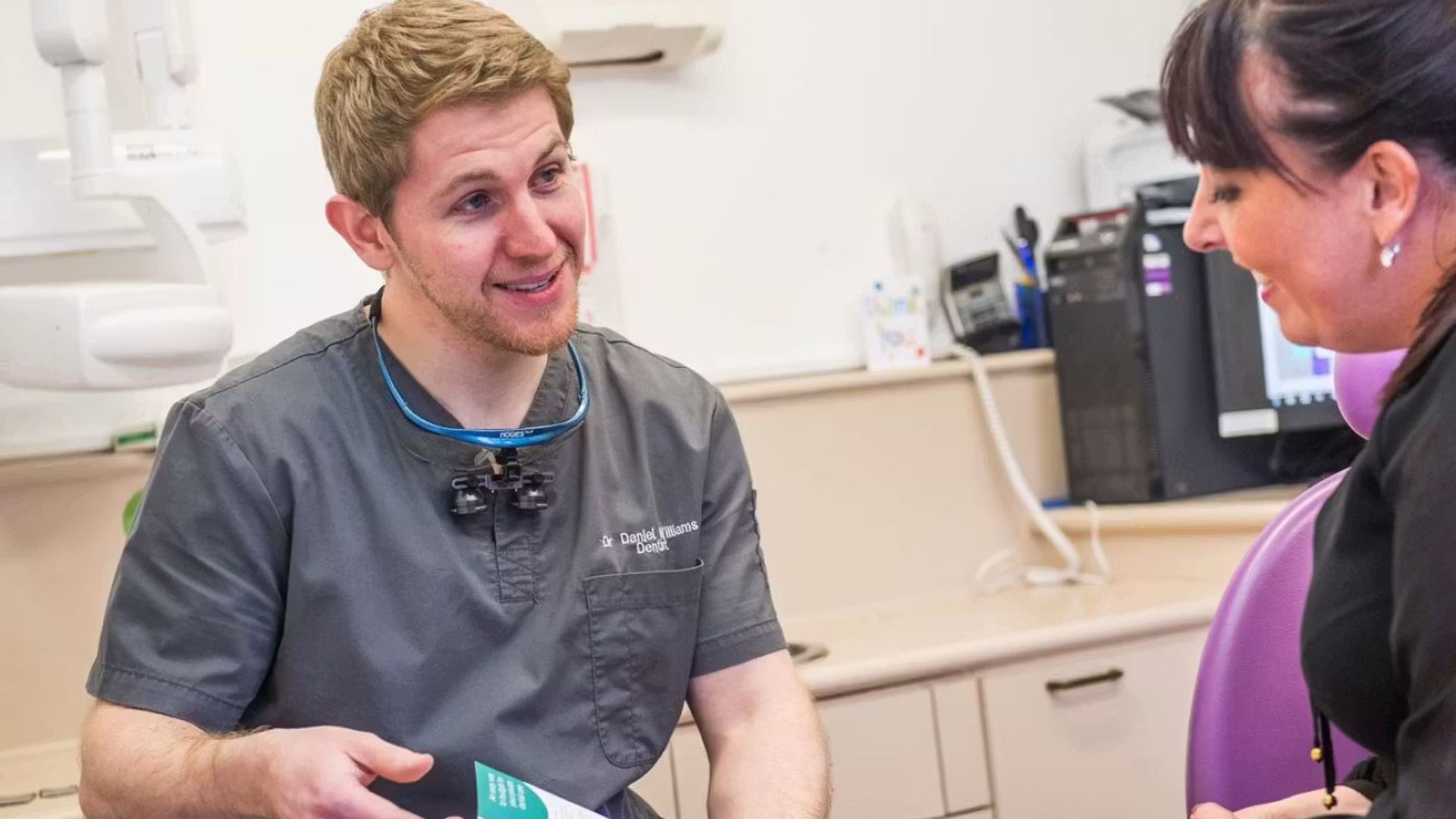 Image of a male clinician showing a document to a female patient and explaining fees.