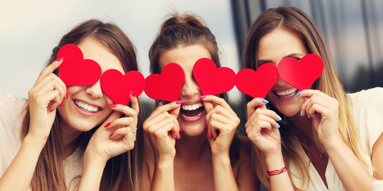 friends smiling while holding cut out hearts over their eyes