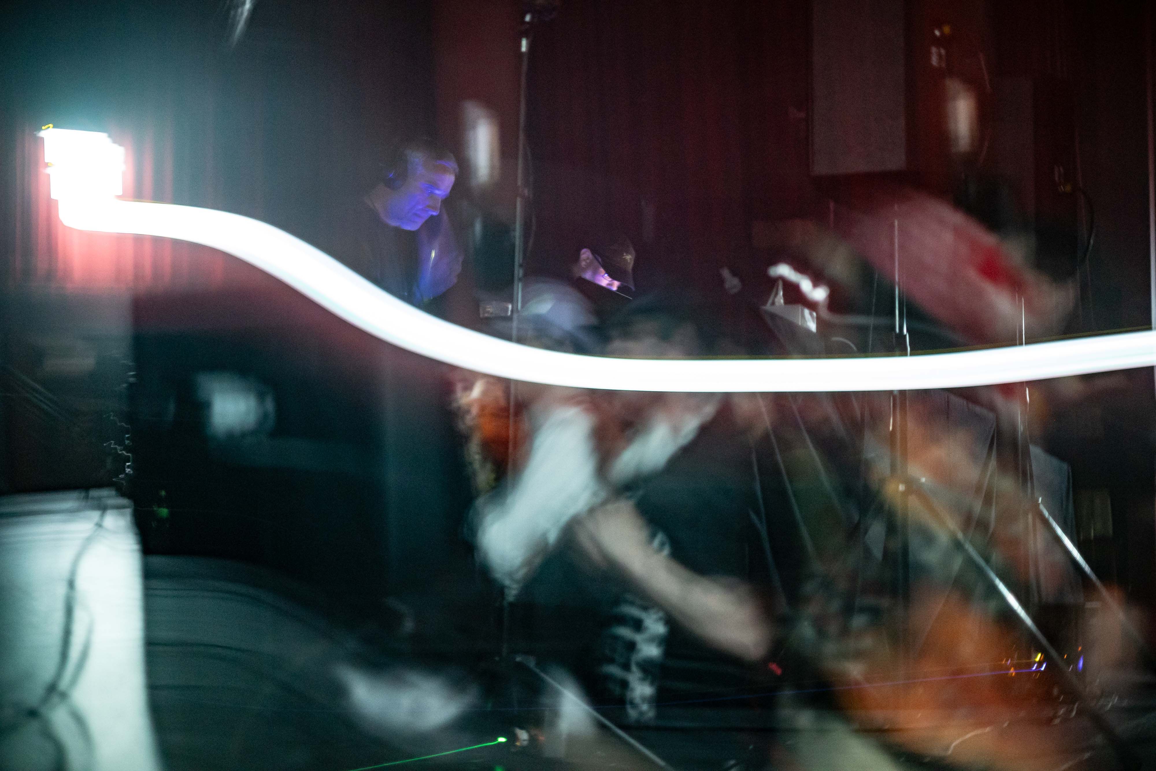 A long exposure showing both the crowd and Autechre performing in a near pitch black environment, but with a giant streak across the frame of an exit sign
