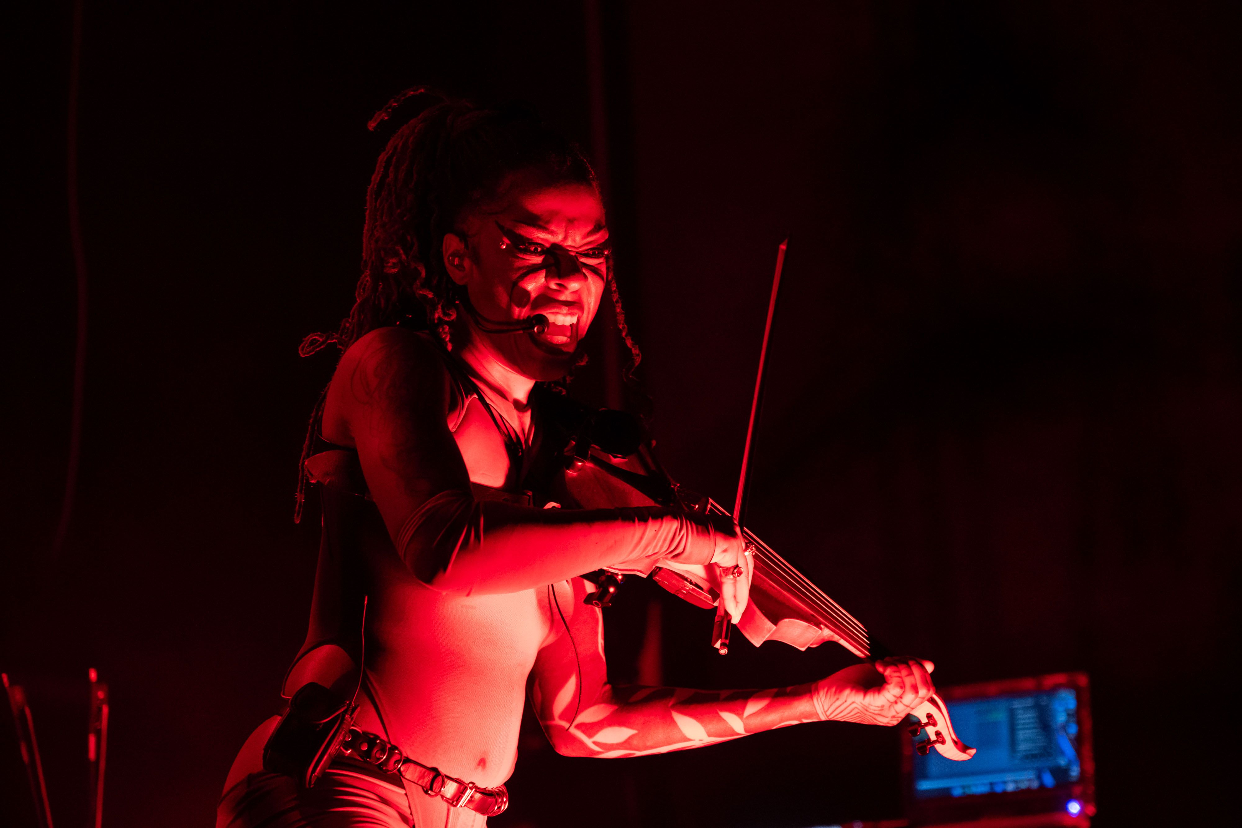 Sudan Archives plays her violin bathed in red light, looking down at the audience