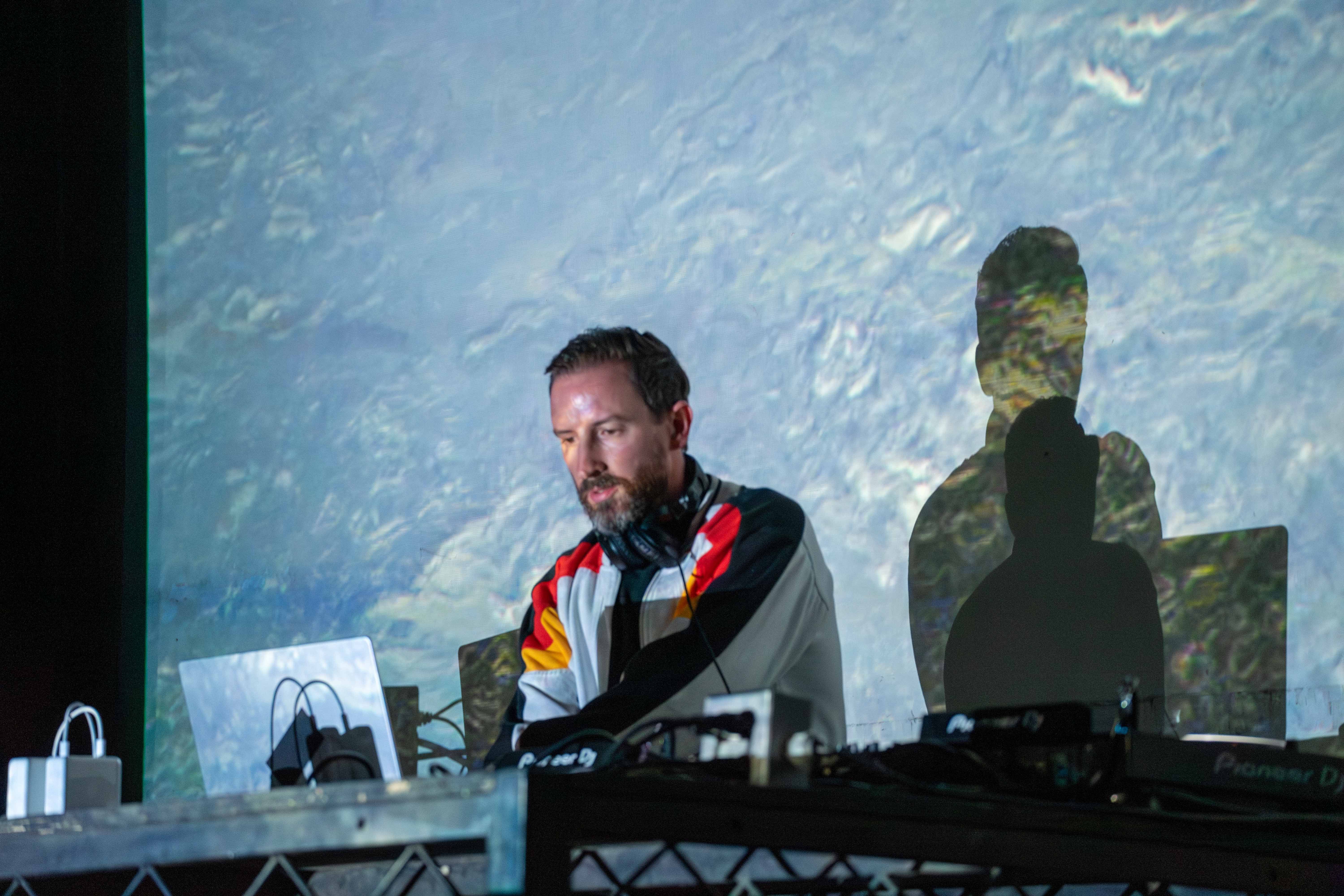 Max Cooper in front of a projected screen behind a laptop