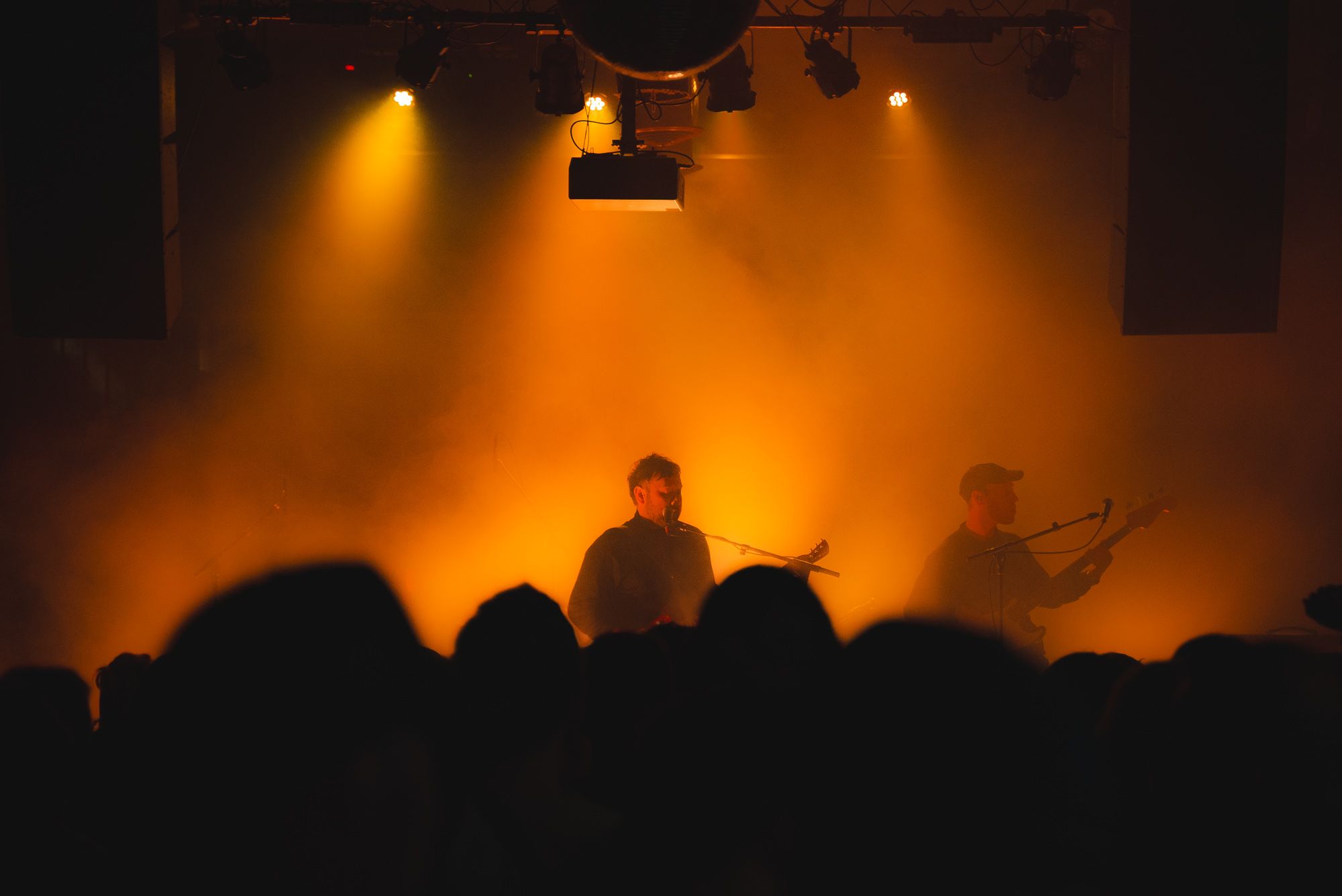 Unknown Mortal Orchestra seen through the crowd performing on stage in a hazy golden light.