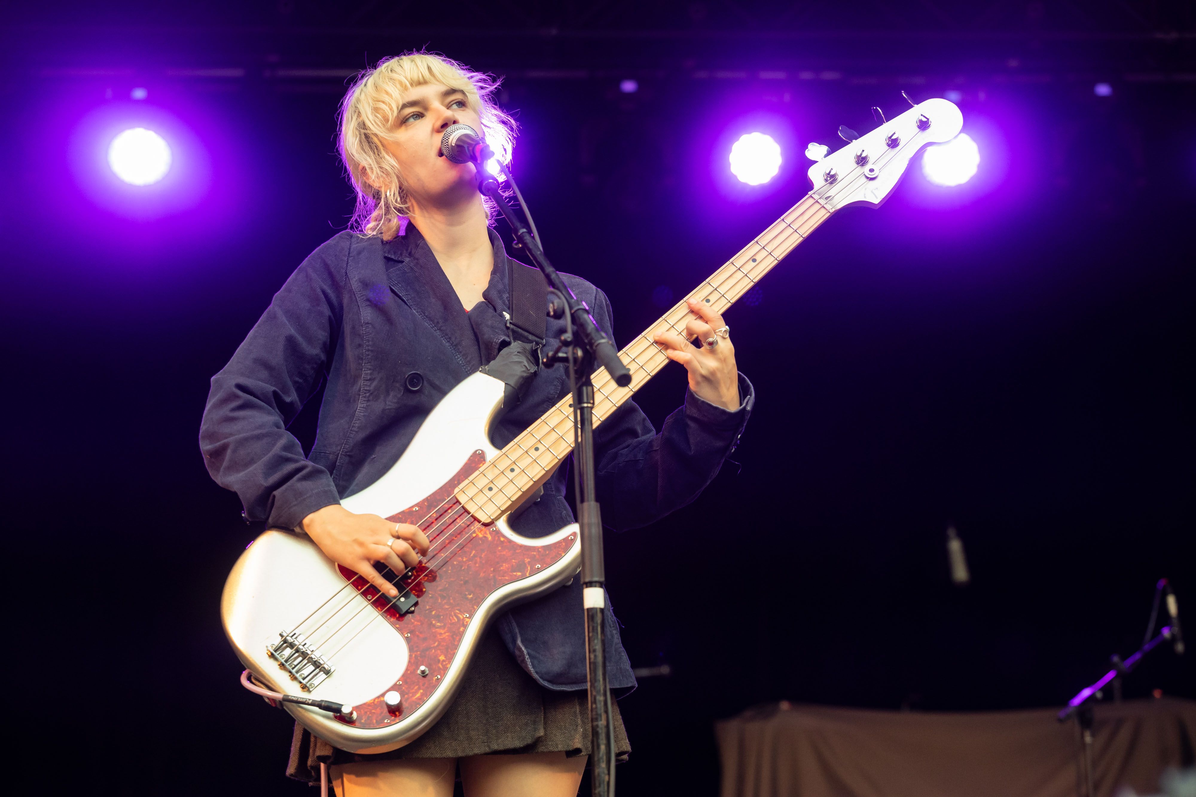 The frontwoman from Mary in the Junkyard plays her bass guitar and sings, backlit by purple lights