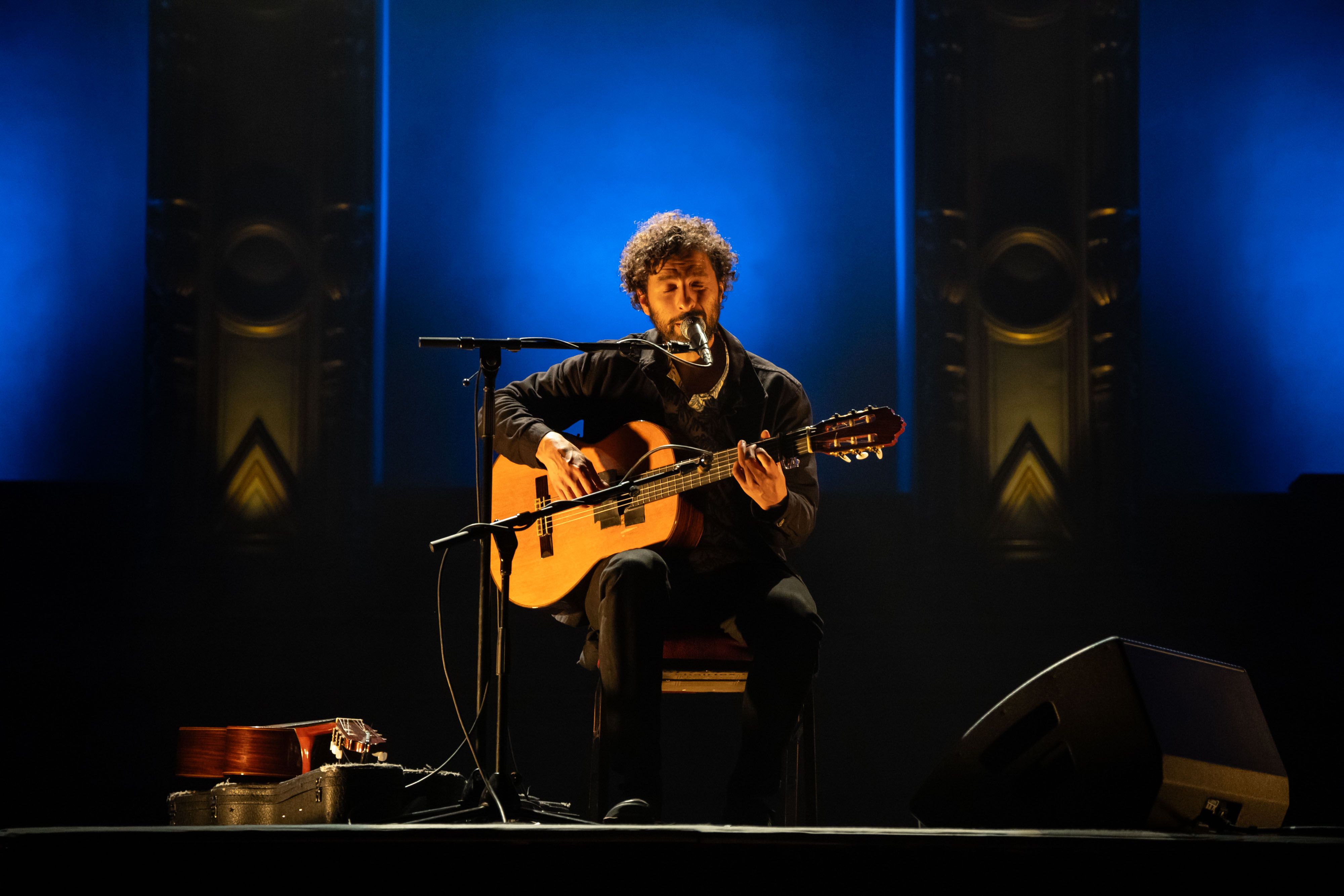 José González sits on the stage of the Orpheum Theatre bathed in yellow light with blue around the columns in the back