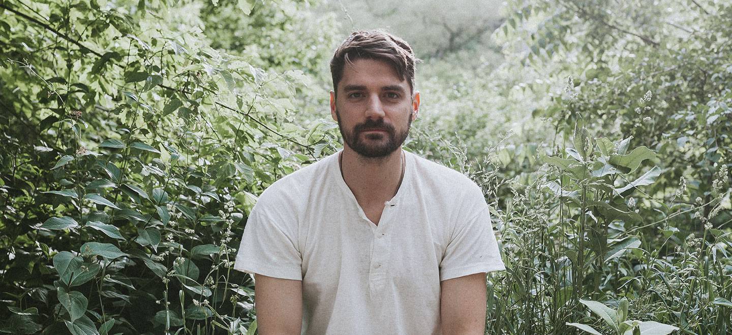 Musician Tim Baker sitting in front of a lot of green plants.