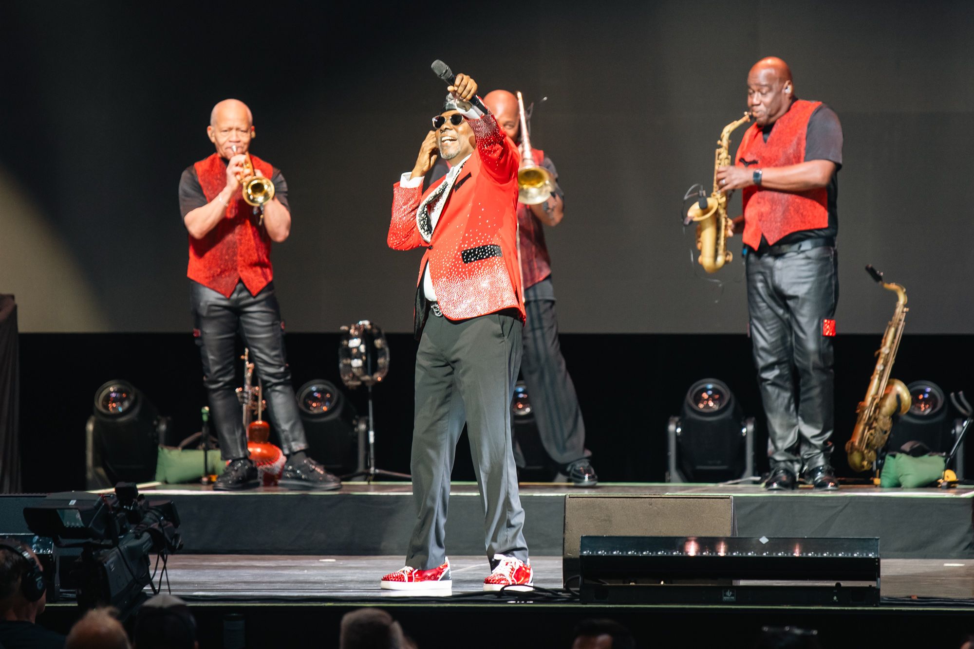 Earth, Wind & Fire playing to a packed audience. Their singer has his arm outreached with a mic for the audience