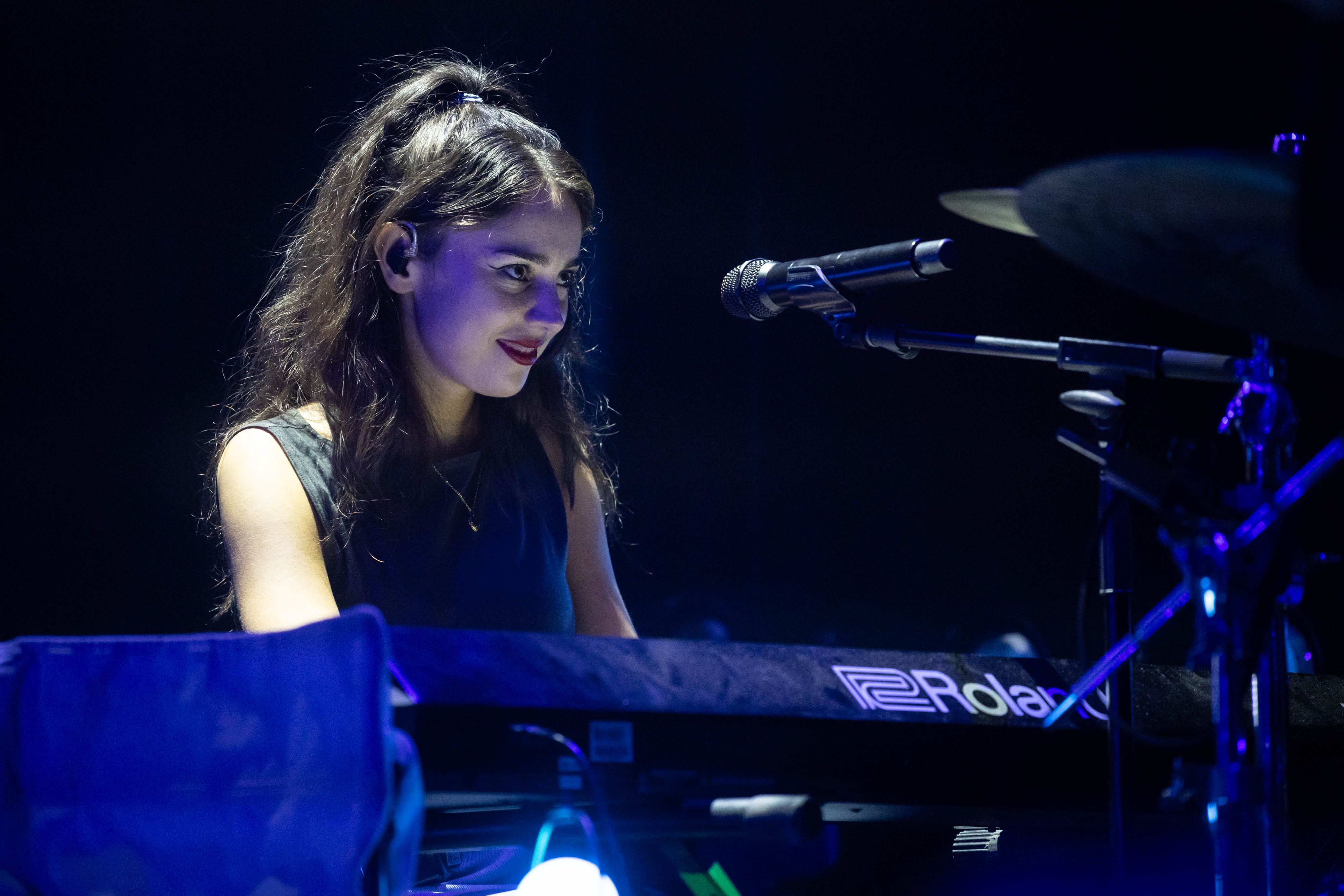 Samia smiles to someone out of frame right with a cheeky grin while playing the piano