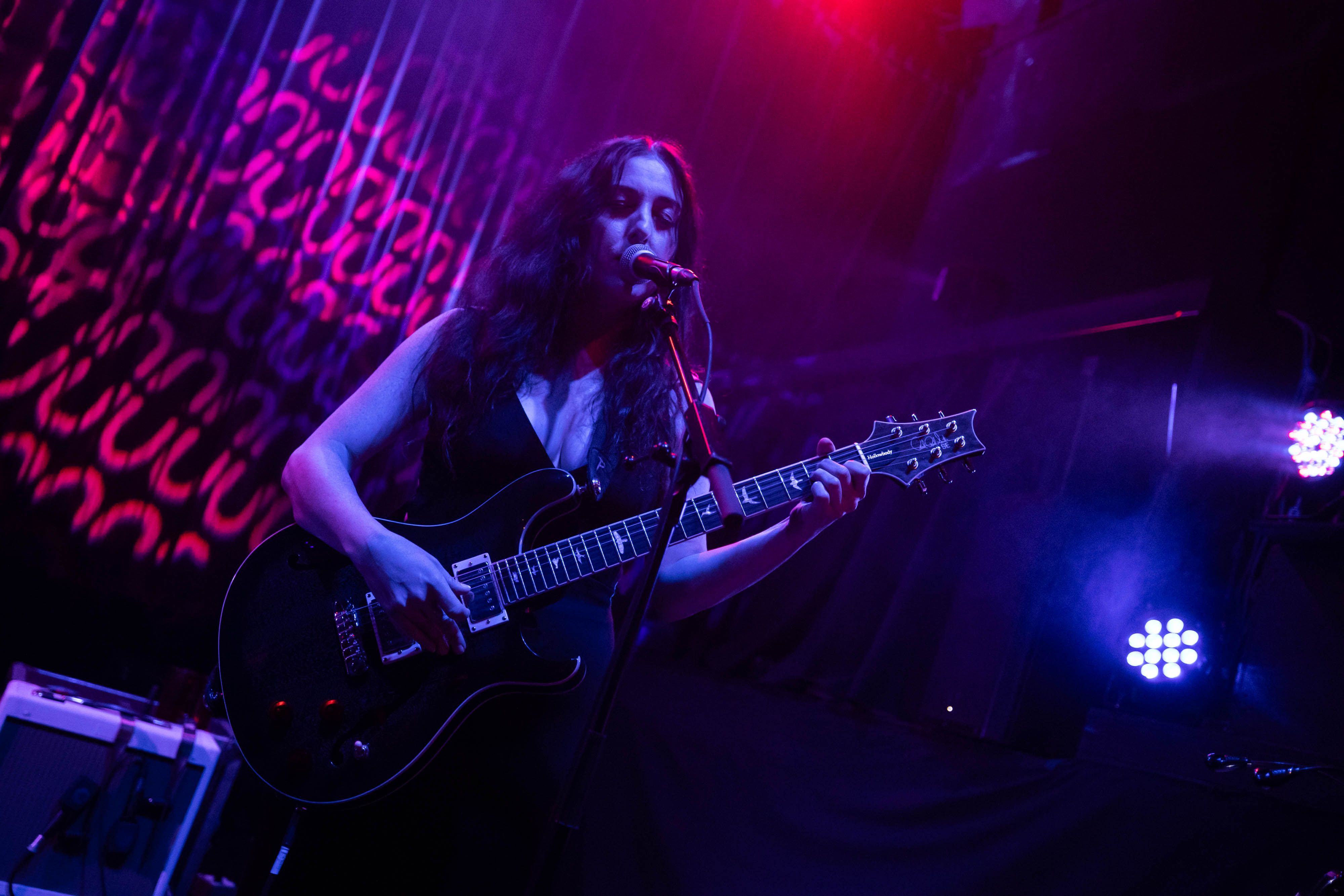 Marissa Nadler is playing guitar on the stage at the Fox lit in blue and backlit by red circles