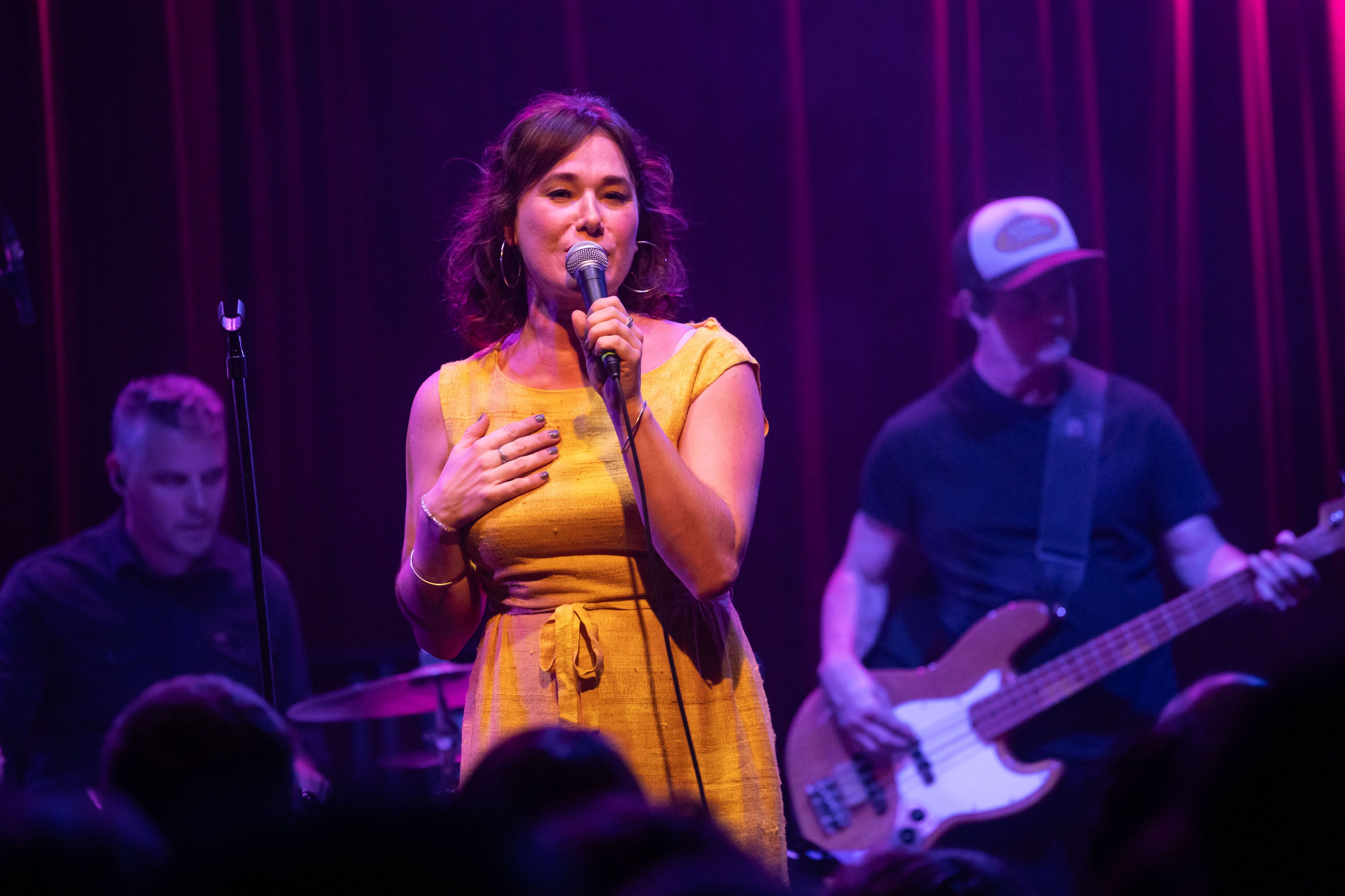 Colleen Rennison is on stage at the Fox Cabaret in a yellow dress showered in purple light