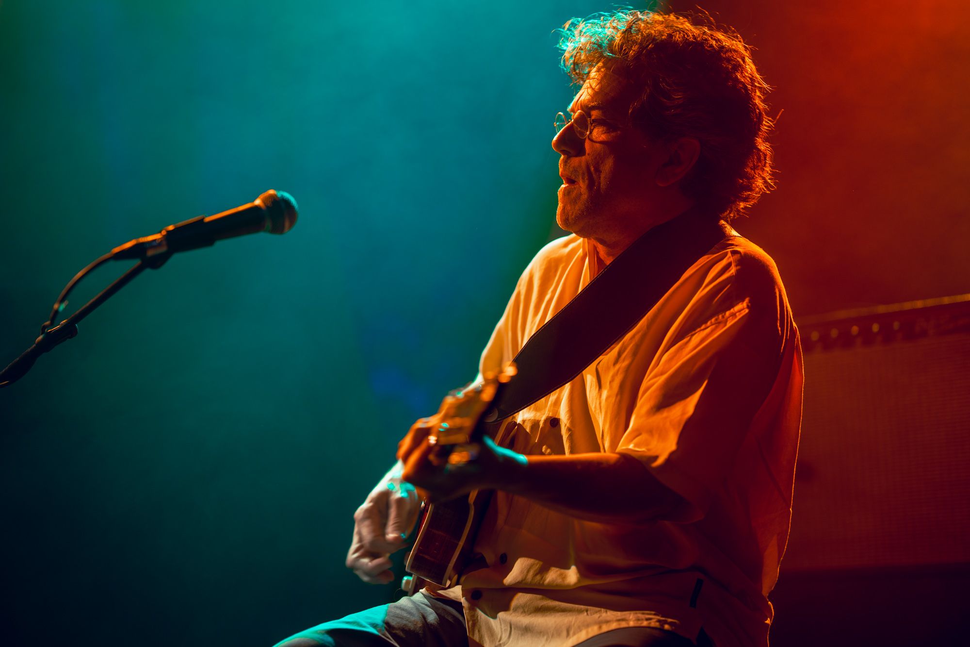 René Lussier playing guitar in front of a mic with a blue and red background