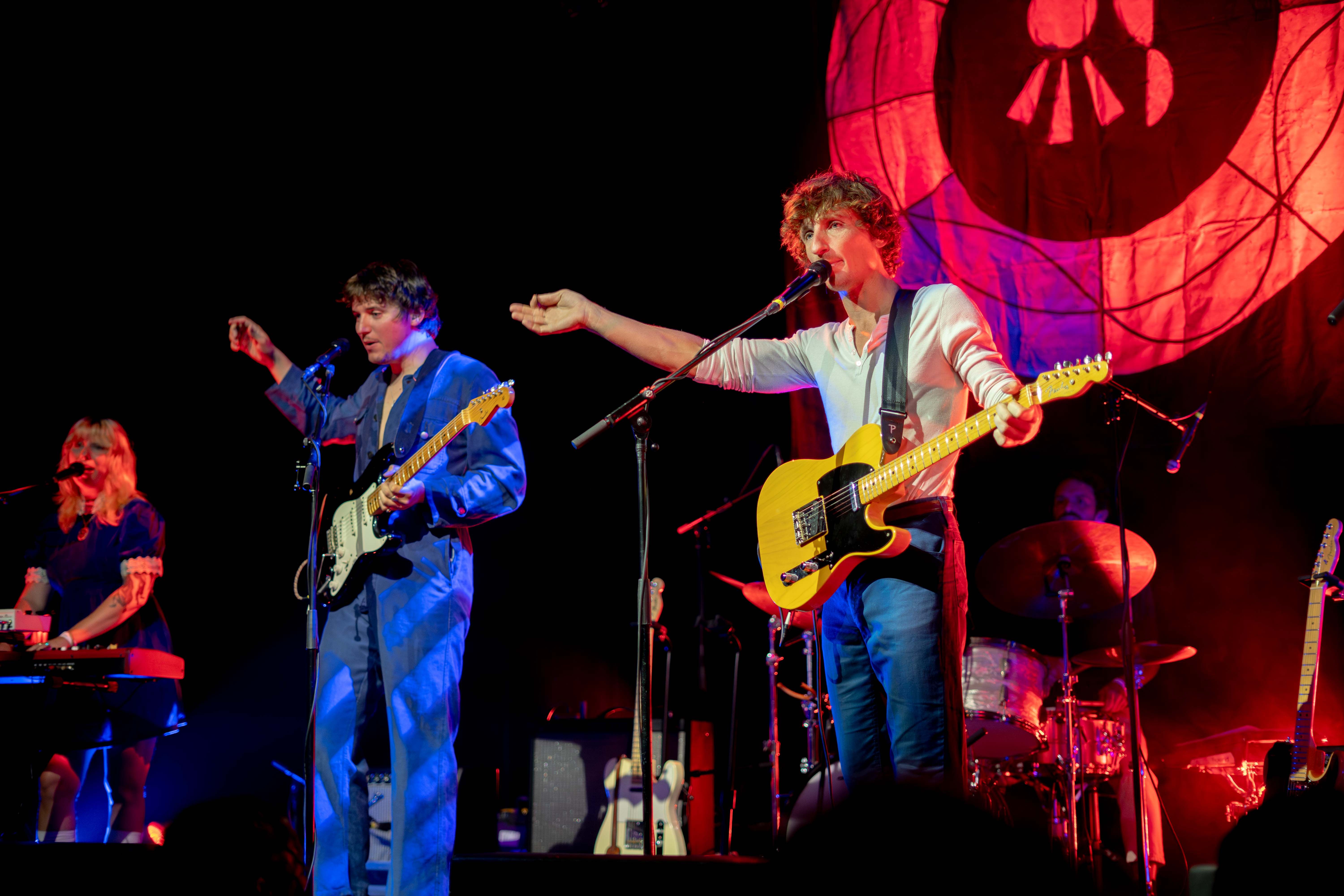 Oracle Sisters band members holding guitars and raising their arm up while singing into a microphone