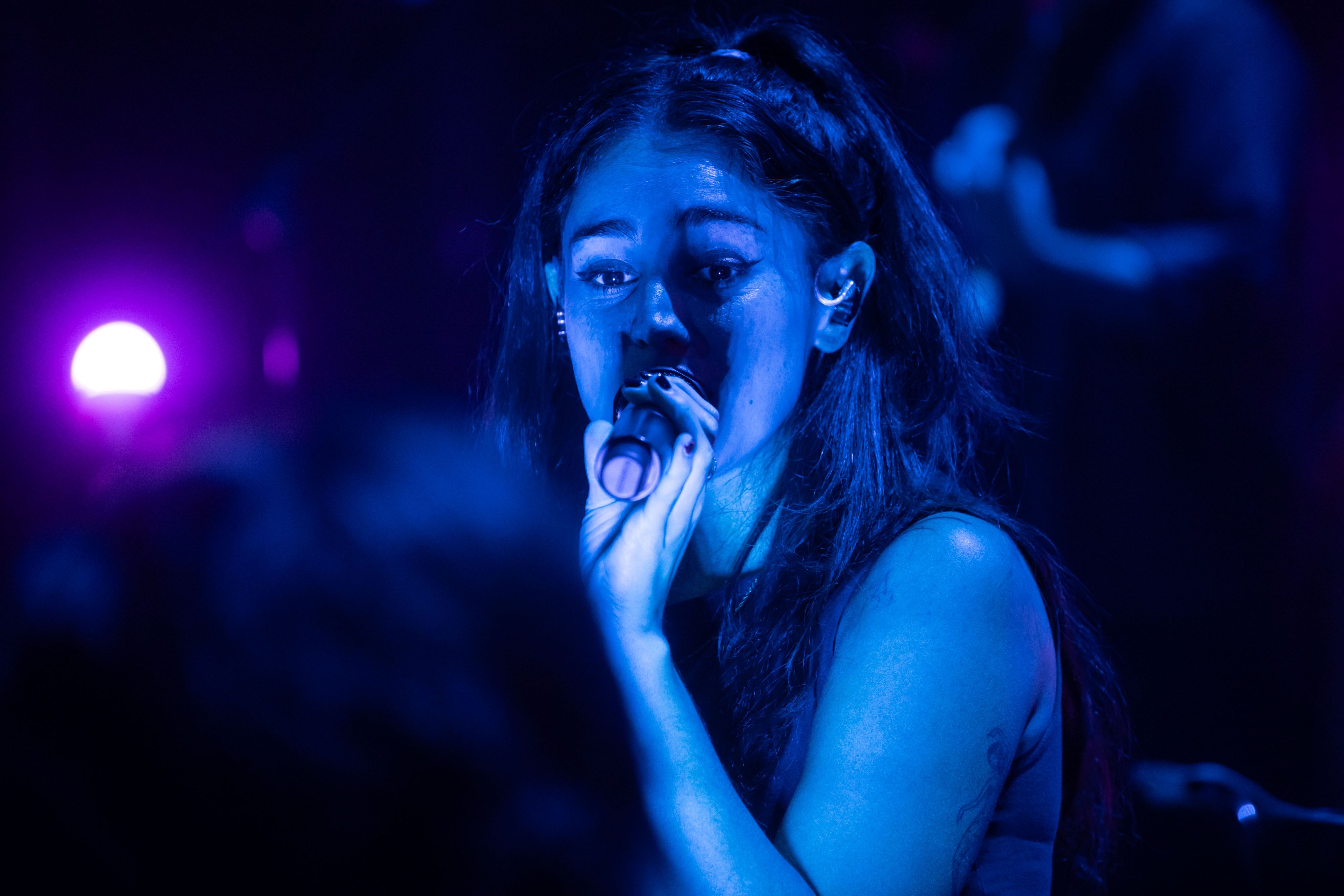 Samia sings into a wireless mic on the stage at the Hollywood Theatre bathed in blue light, staring just away from us