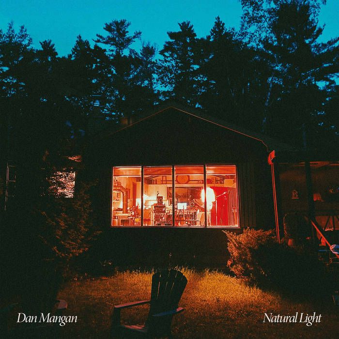 Cover of the album Natural Light by Dan Mangan showing the warm inside of a cabin seen from outside at dusk.