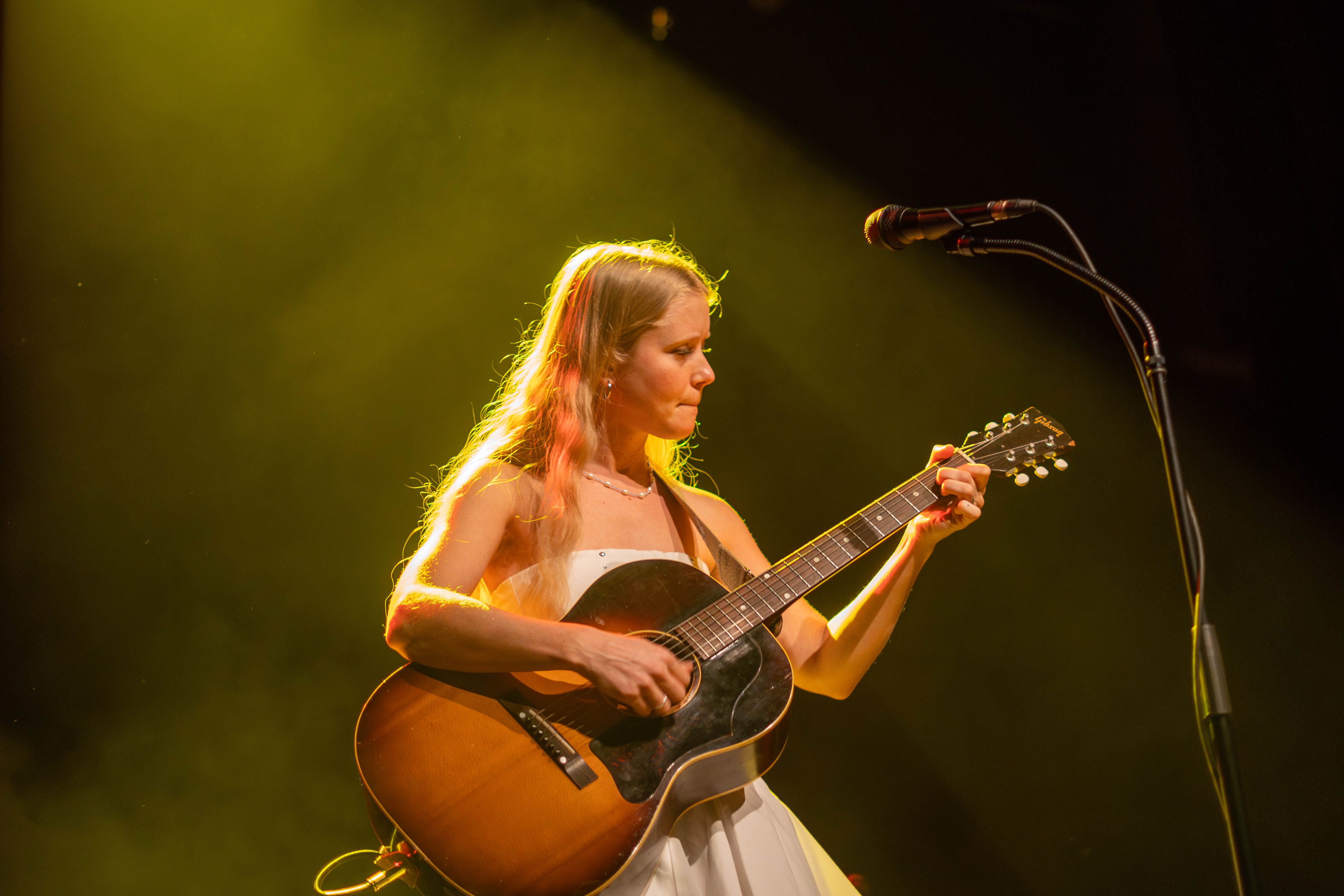 Alice Phoebe Lou playing an acoustic guitar standing in front of a microphone