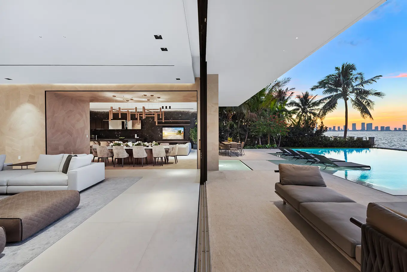 Seamless indoor-outdoor living space with open-concept dining and living area flowing to infinity pool with stunning Miami skyline views at sunset