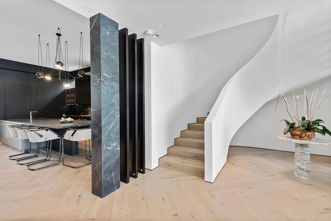 Elegant dining room with modern chandelier and floating staircase featuring vertical black slats