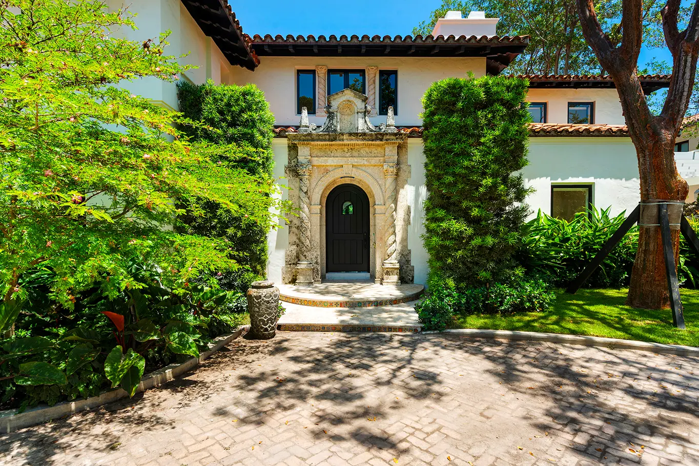Grand arched entrance with ornate wrought iron doors, stone pillars, and lush tropical foliage