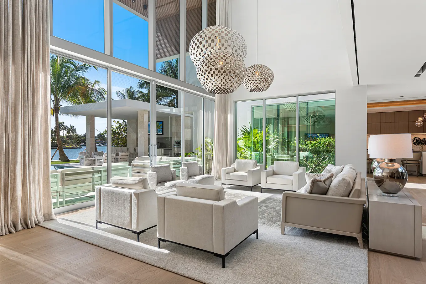 Double-height living room with floor-to-ceiling windows, designer pendant lighting, and seamless indoor-outdoor connection to pool