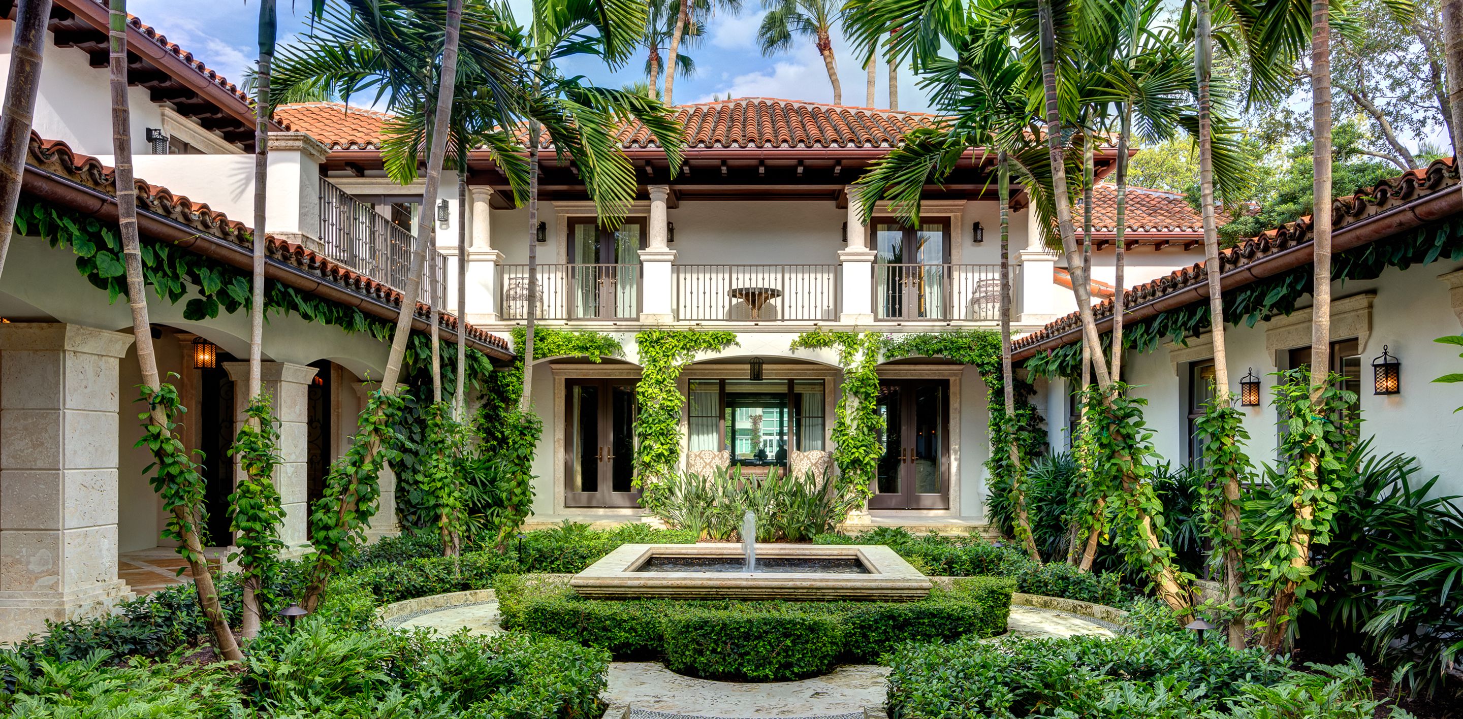 Spanish Colonial estate with terracotta tile roof, two-story architecture, and lush interior courtyard with central fountain in Miami
