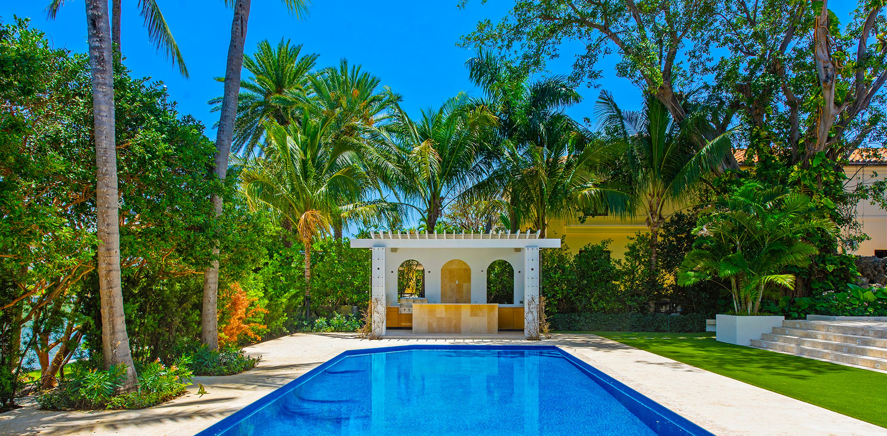 Spanish Mediterranean estate with white arched poolside pavilion, vibrant blue pool, and lush tropical gardens in Miami