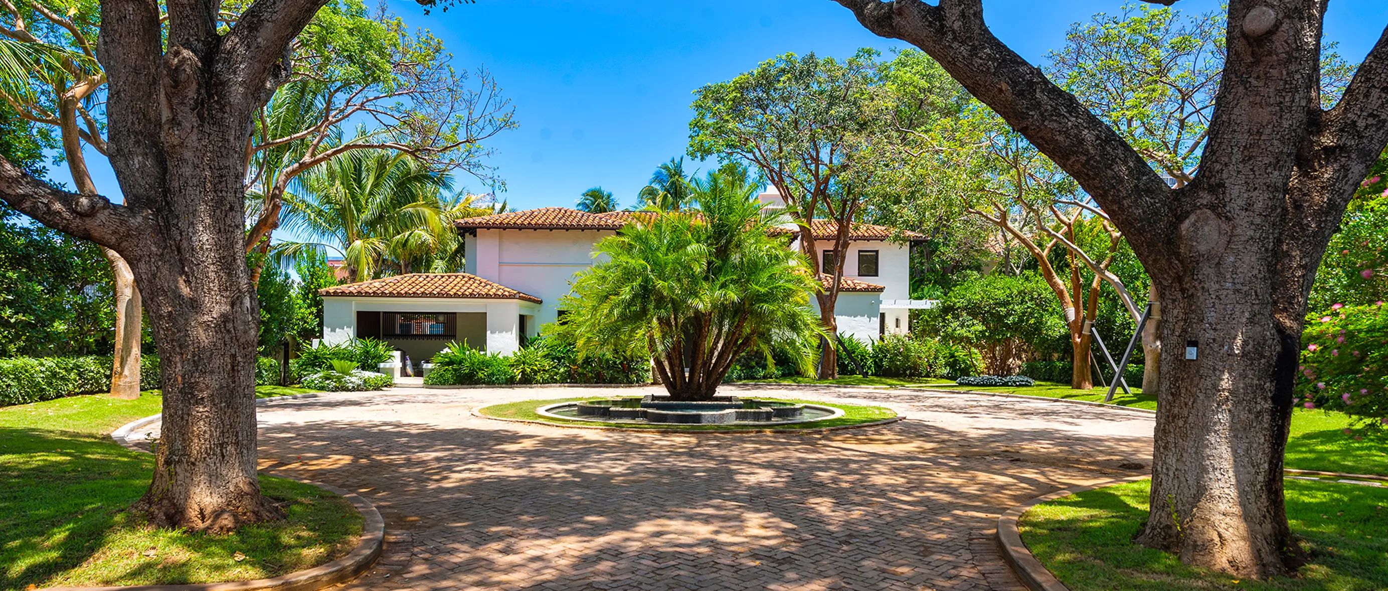 Sweeping circular driveway leading to Spanish estate with manicured lawn and mature palm trees
