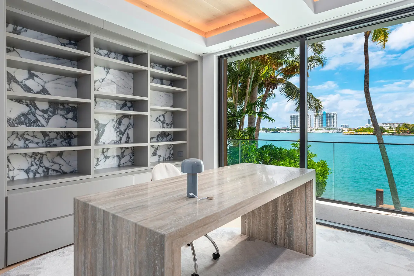 Waterfront home office with marble-backed shelving, custom wood desk, and panoramic ocean and Miami skyline views