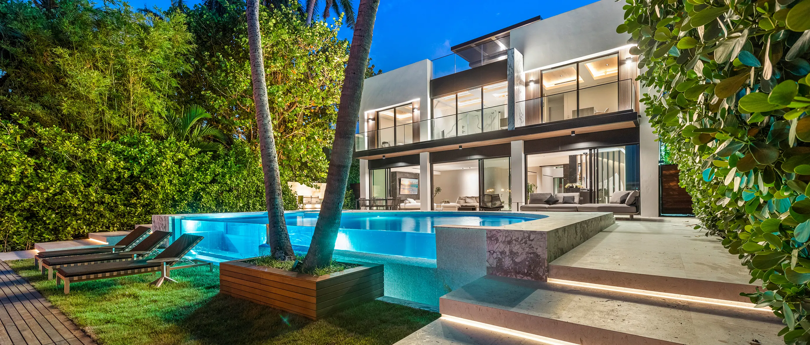 Stunning two-story contemporary residence at dusk with glass infinity pool, palm trees, and expansive outdoor entertaining areas