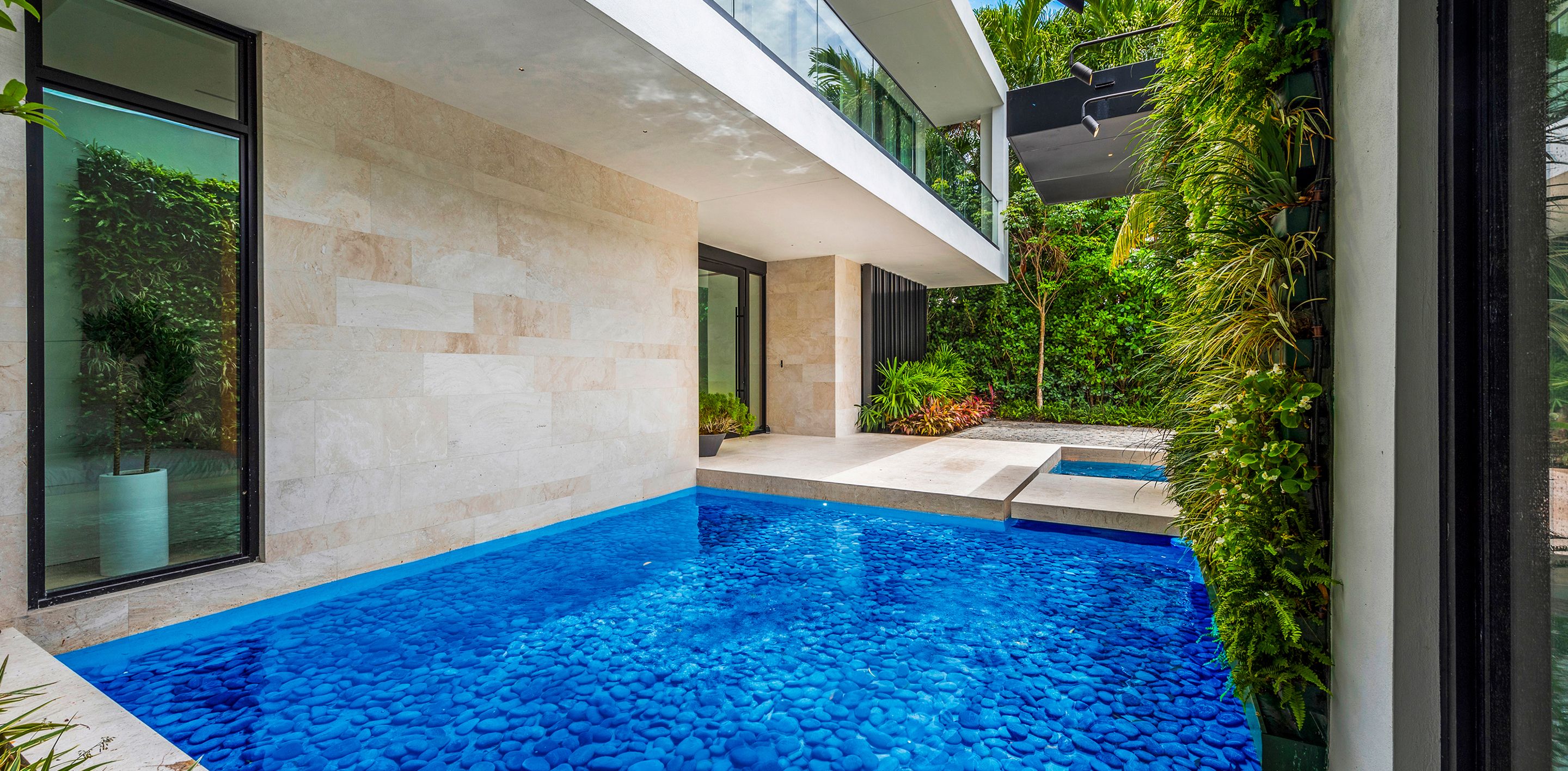 Modern luxury waterfront residence with vibrant blue infinity pool, contemporary architecture, and lush tropical landscaping
