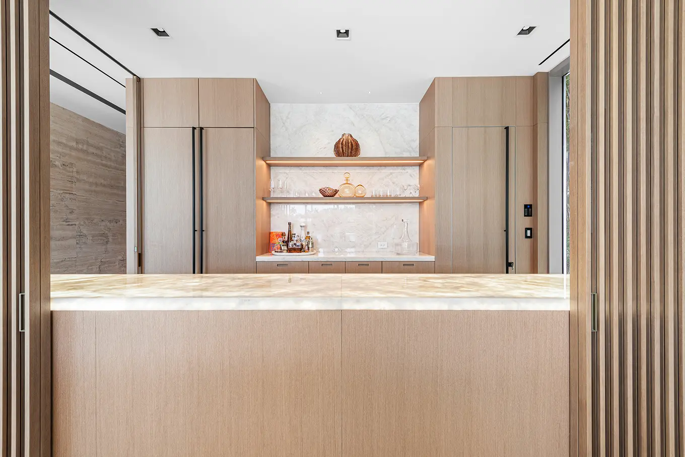 Modern home bar with marble countertops, glass shelving, and contemporary design details