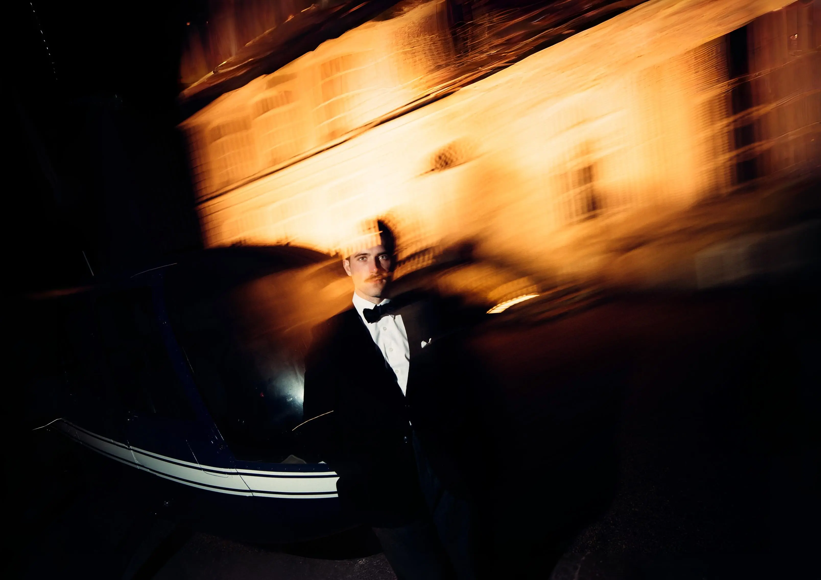 Person in a tuxedo standing in front of a helicopter and a castle at night.