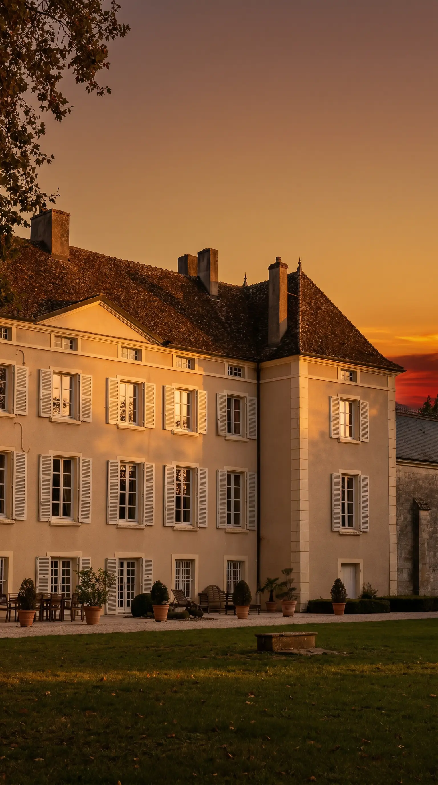 Sunny facade of a Burgundy chateau with white shutters, surrounded by a garden and terrace.