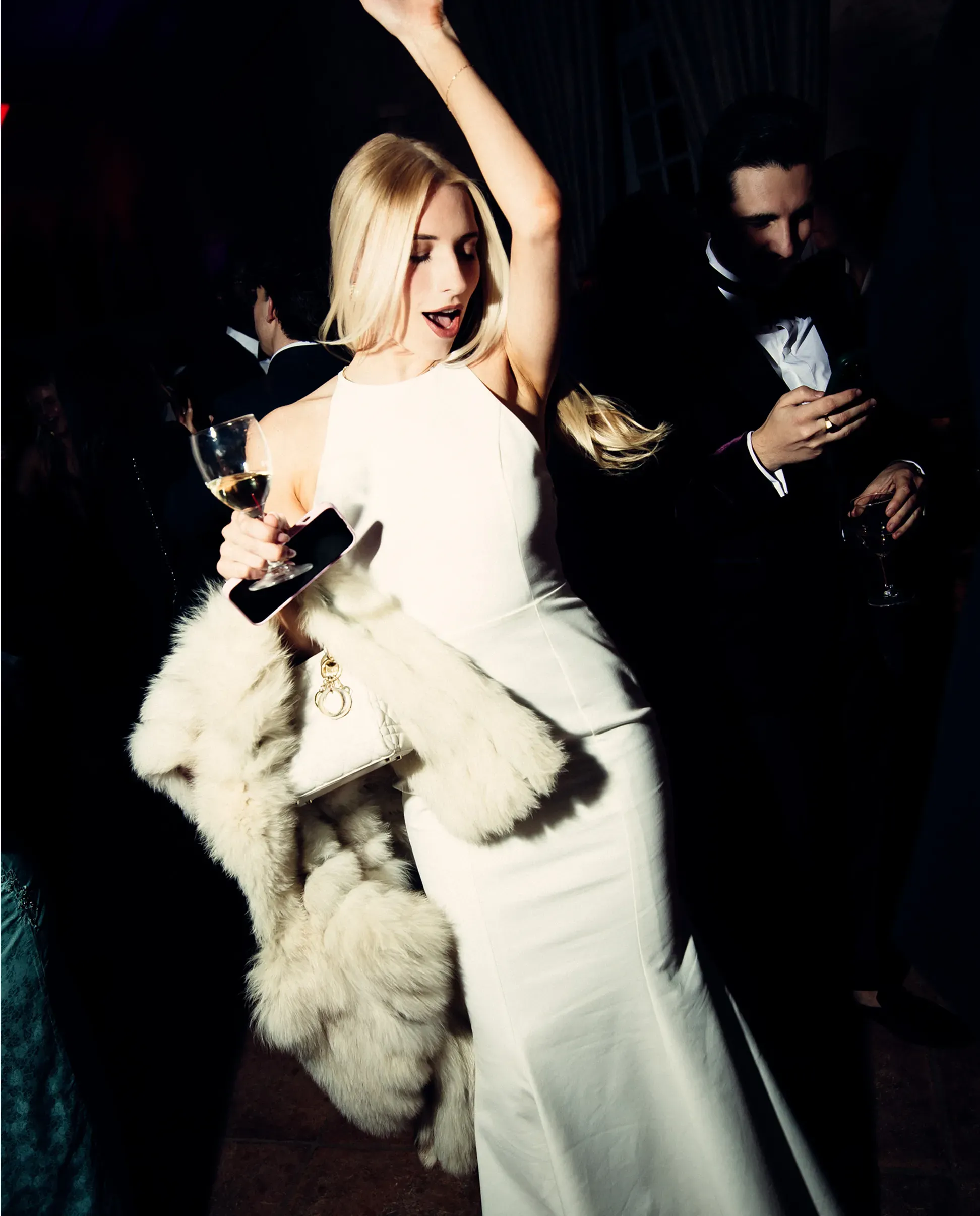 A female club member in a white dress dancing with a glass of champagne in hand.