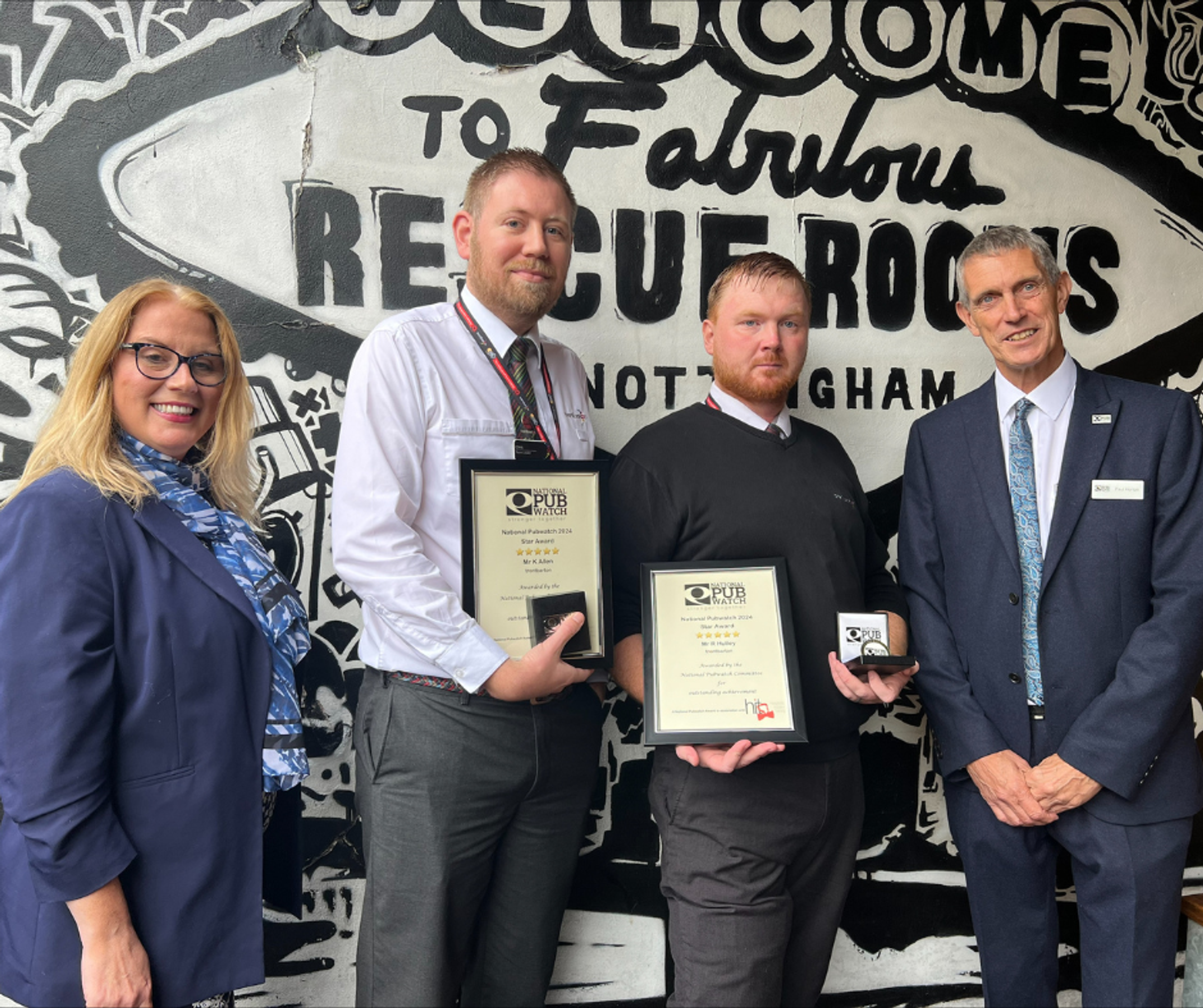 Four people posing with certificates in front of the Rescue Rooms sign in Nottingham
