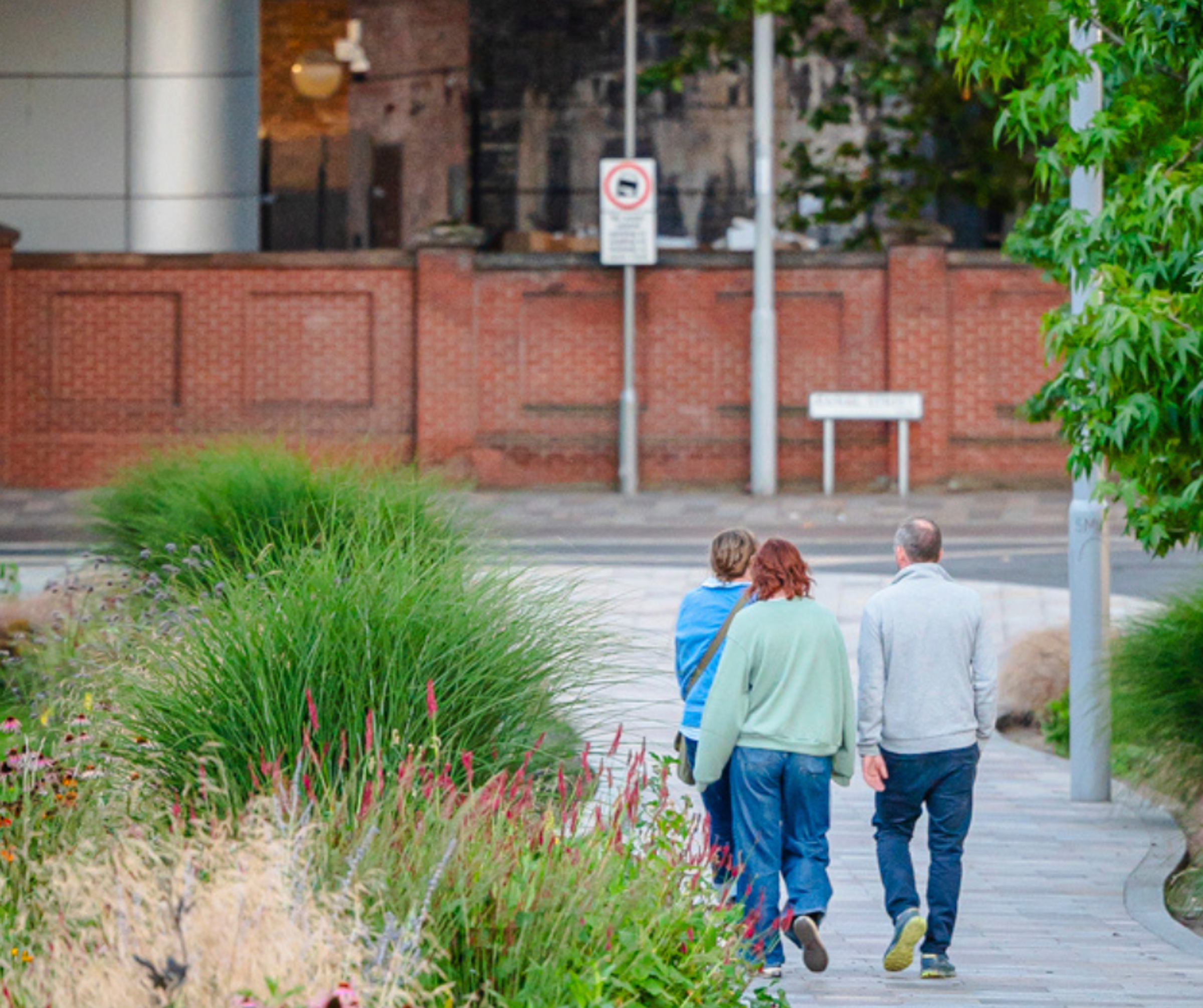 Three people walk near Broadmarsh Car Park, Nottingham among grasses and flowers
