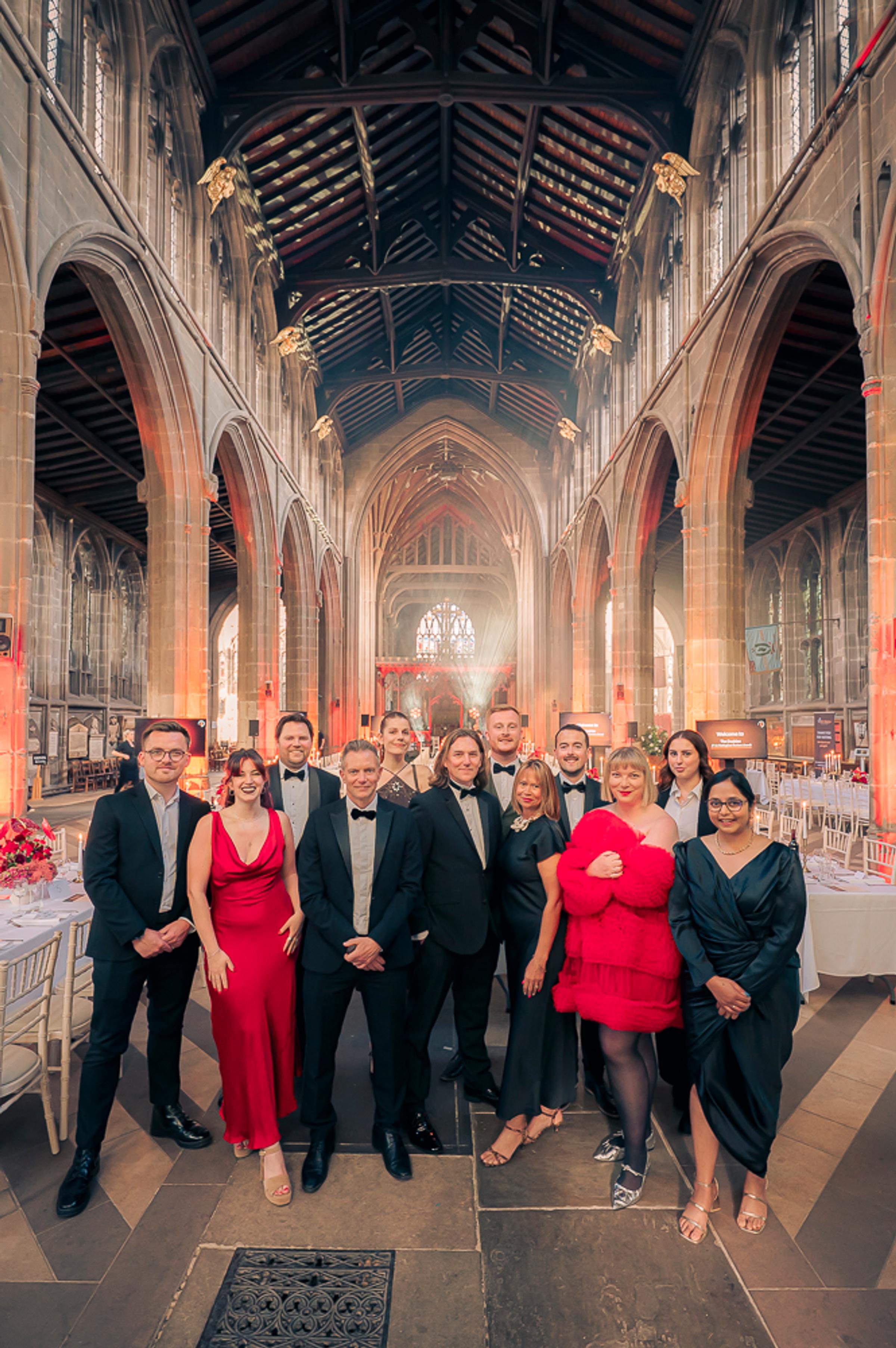 It's in Nottingham team posing in glamorous outfits in a church set for an awards dinner. The colour theme is red and black.
