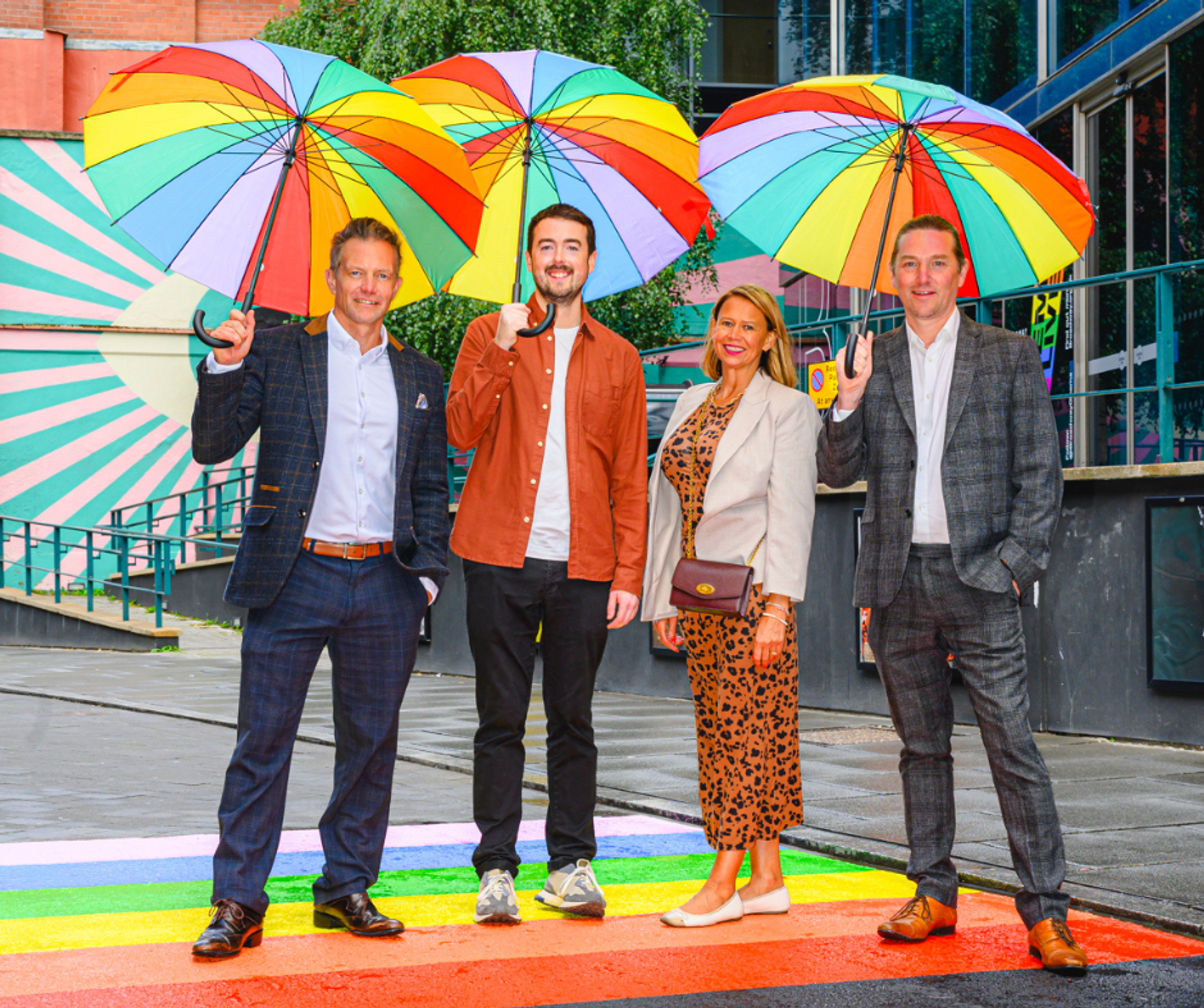 Four people on Hockley's rainbow road in Nottingham, with 3 holding rainbow umbrellas