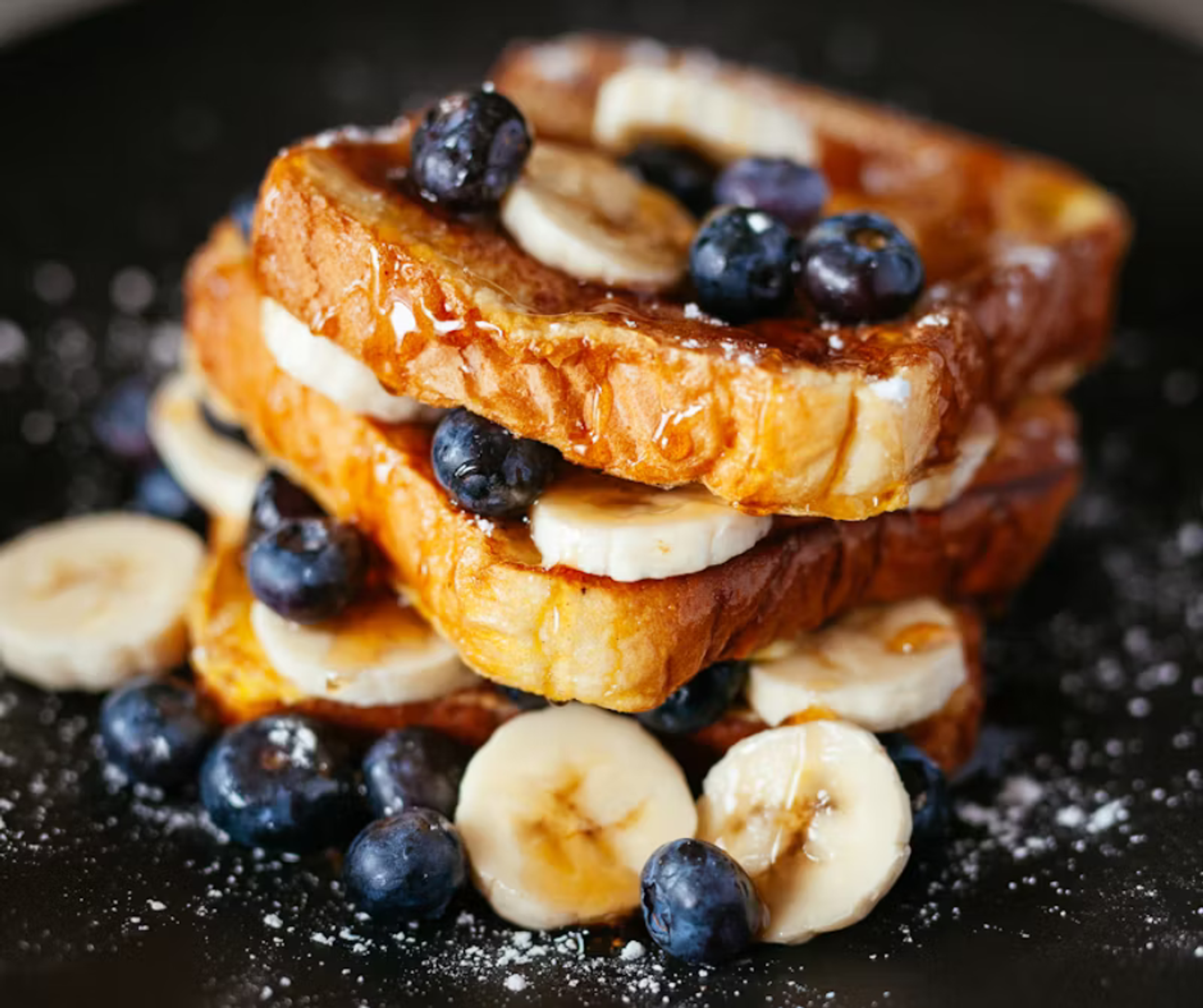 A close up of french toast with bananas, blueberries and syrup