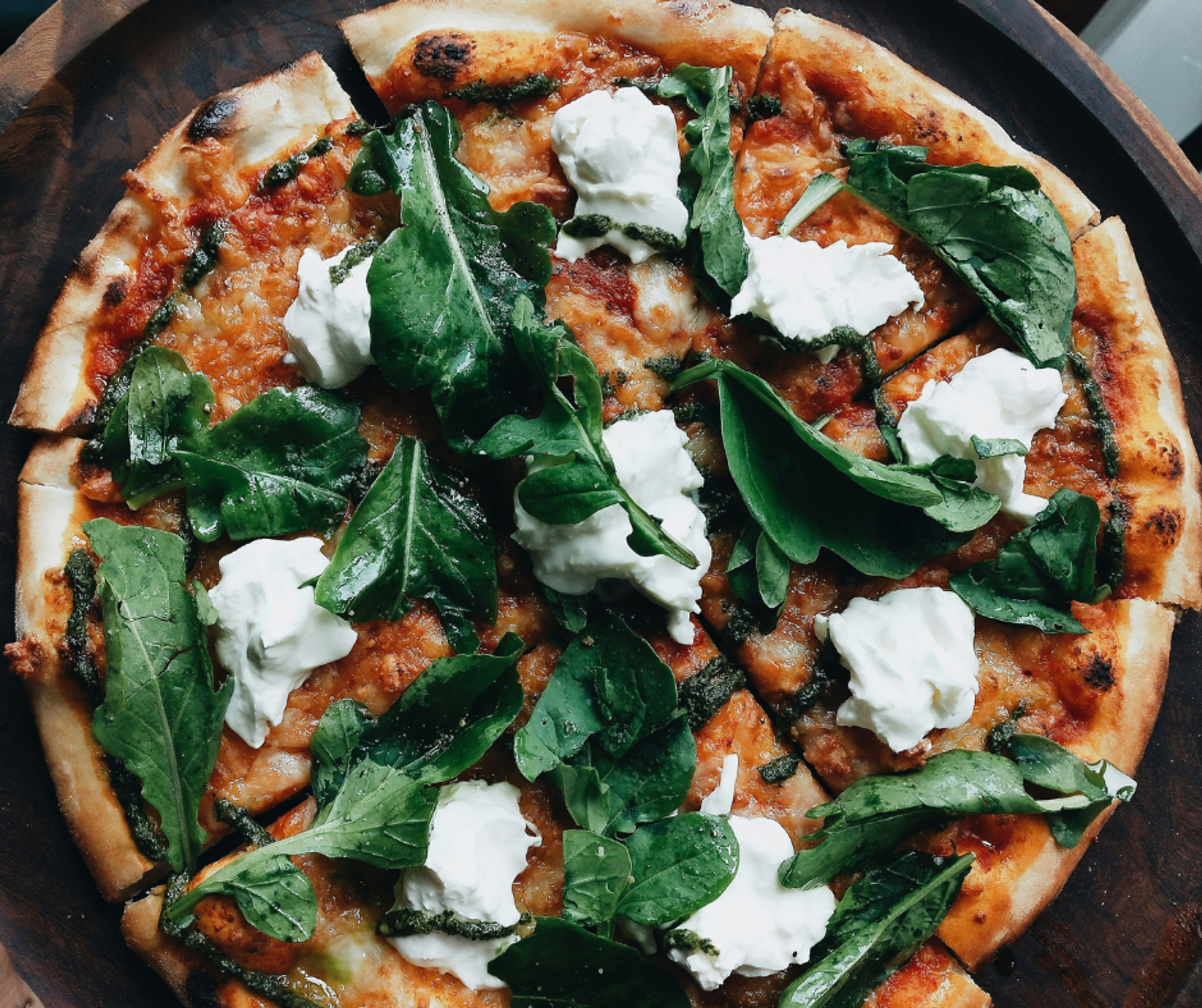 An overhead photo of a pizza with cheese and green leaves